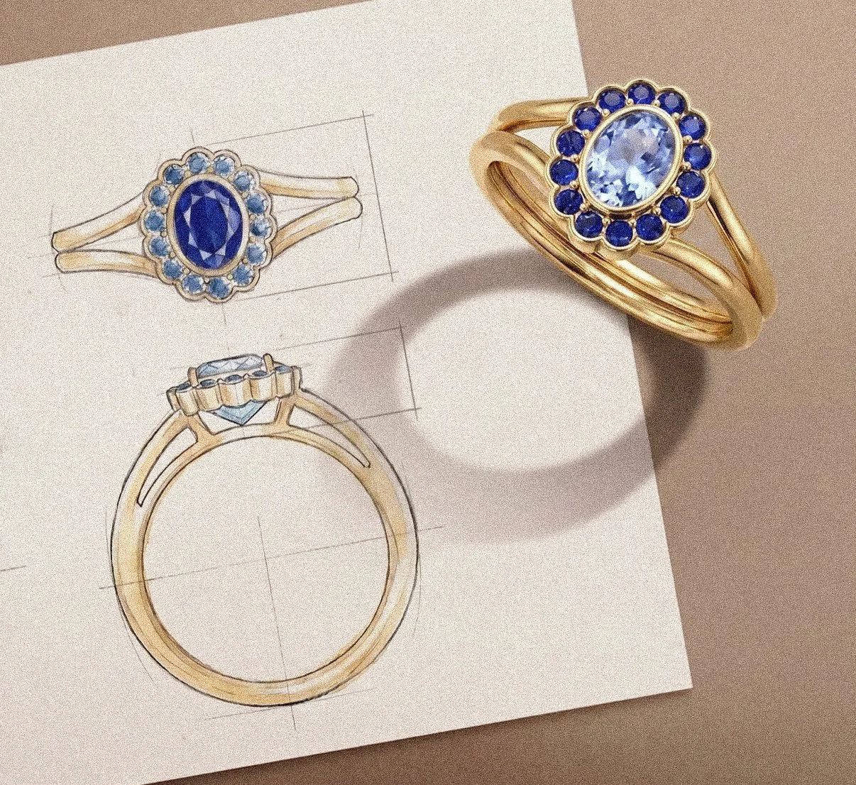 Gold ring with a large oval blue gemstone surrounded by smaller blue gemstones, sitting on a sketch of the ring design.