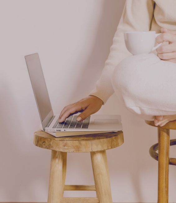 Persona usando una laptop en una mesa de madera, sosteniendo una taza blanca.