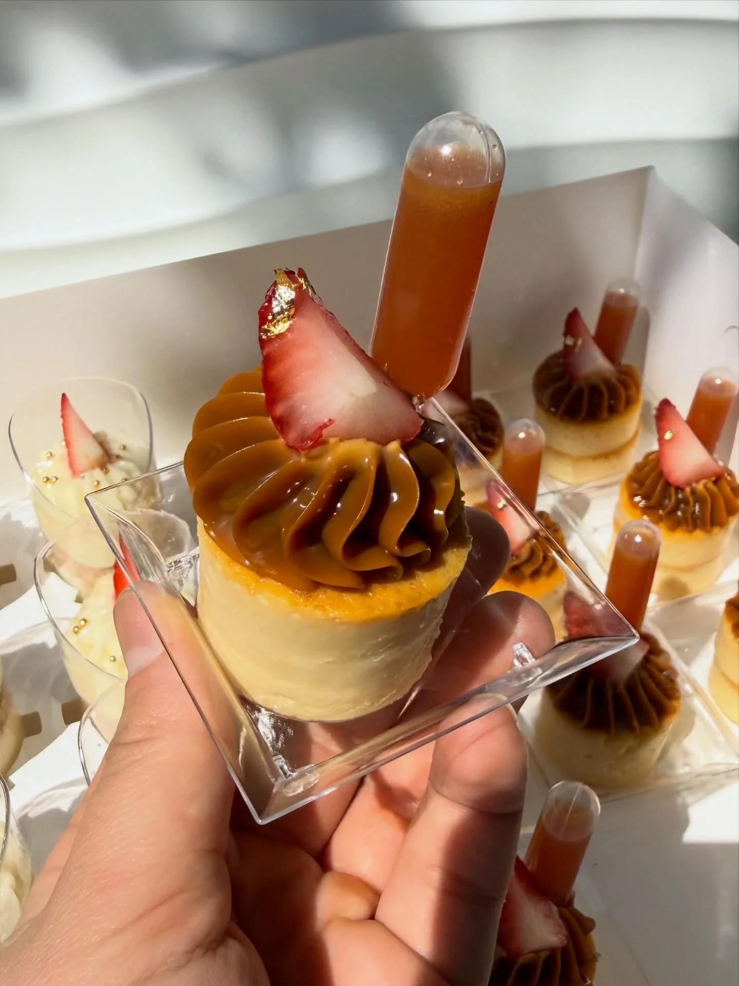 Varias postres decorados con fresas en un mostrador, incluyendo uno en una mano con glaseado de caramelo y una fresa decorativa.