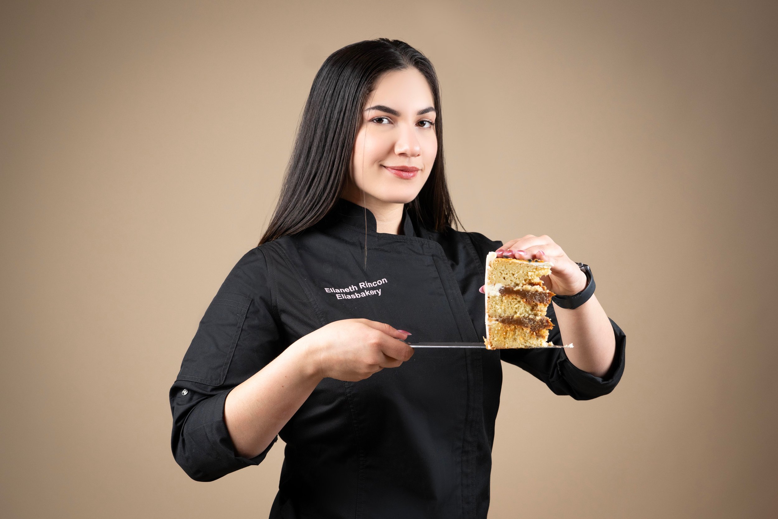 Una mujer con uniforme de chef que sostiene un plato con un pastel de múltiples capas.