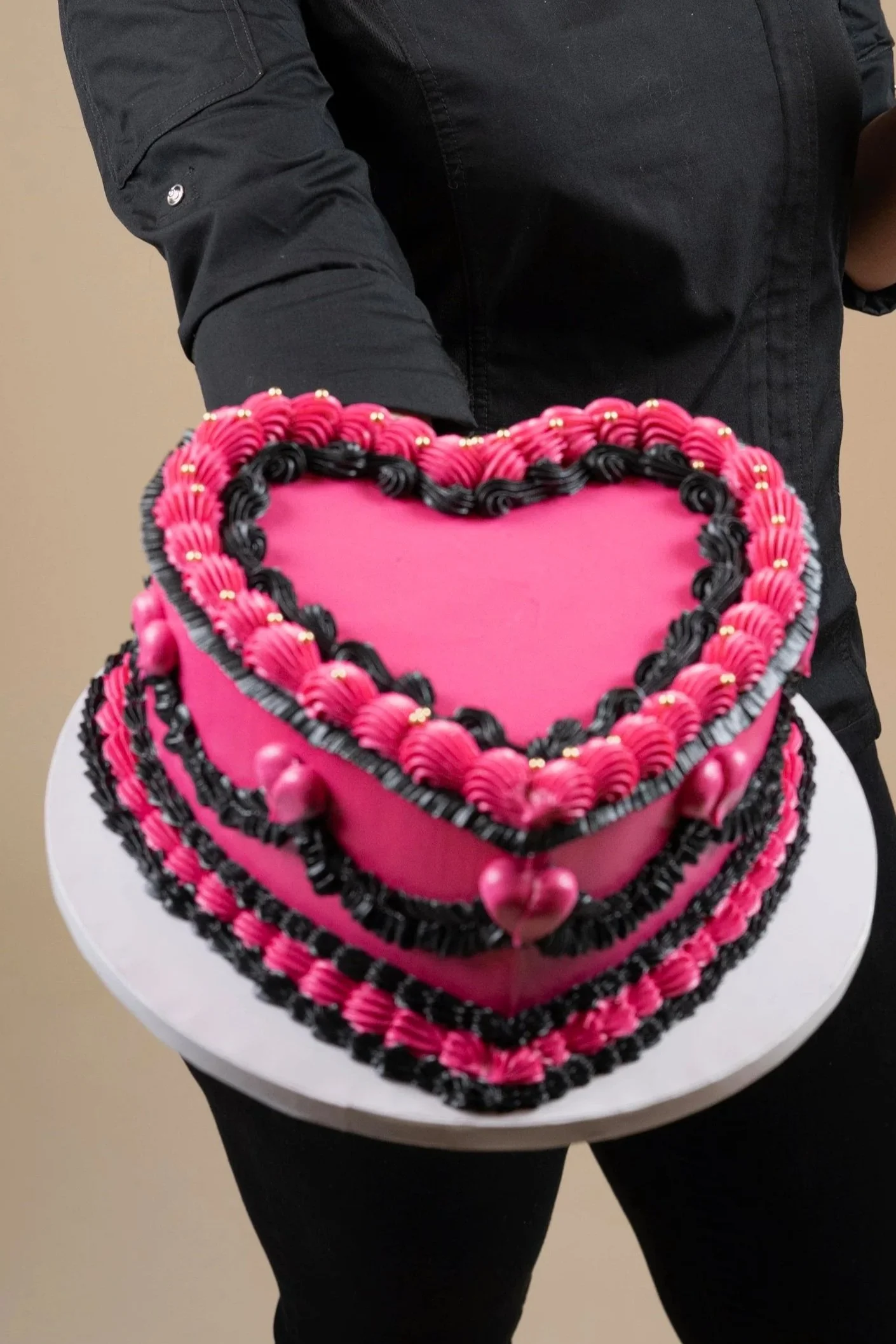 Persona sosteniendo un pastel de corazón decorado con glaseado rosa, negro y dorado.