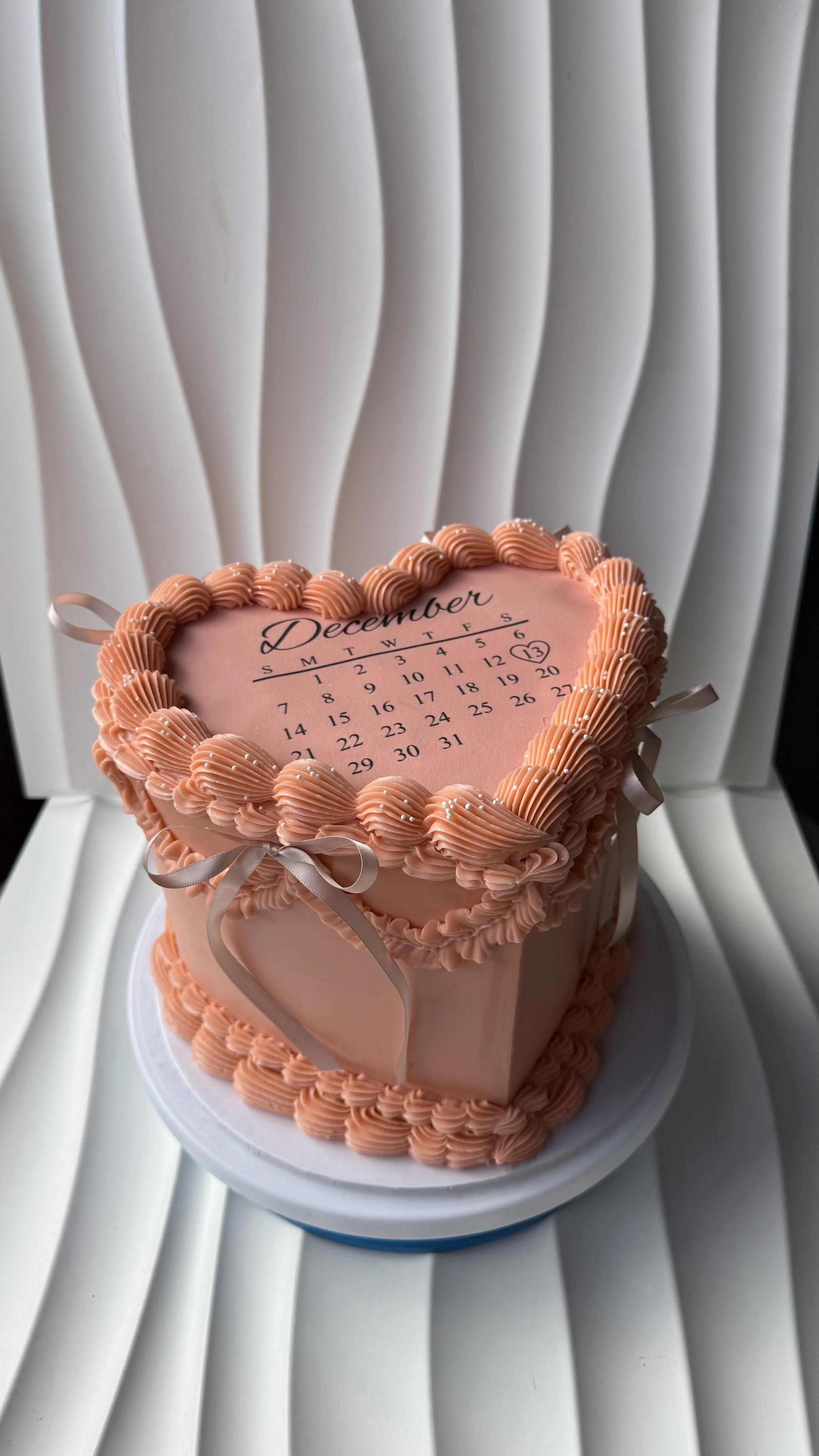 Pastel en forma de corazón con decoración rosa y calendario de diciembre en la parte superior, con el símbolo de un corazón y el número 13 resaltados.