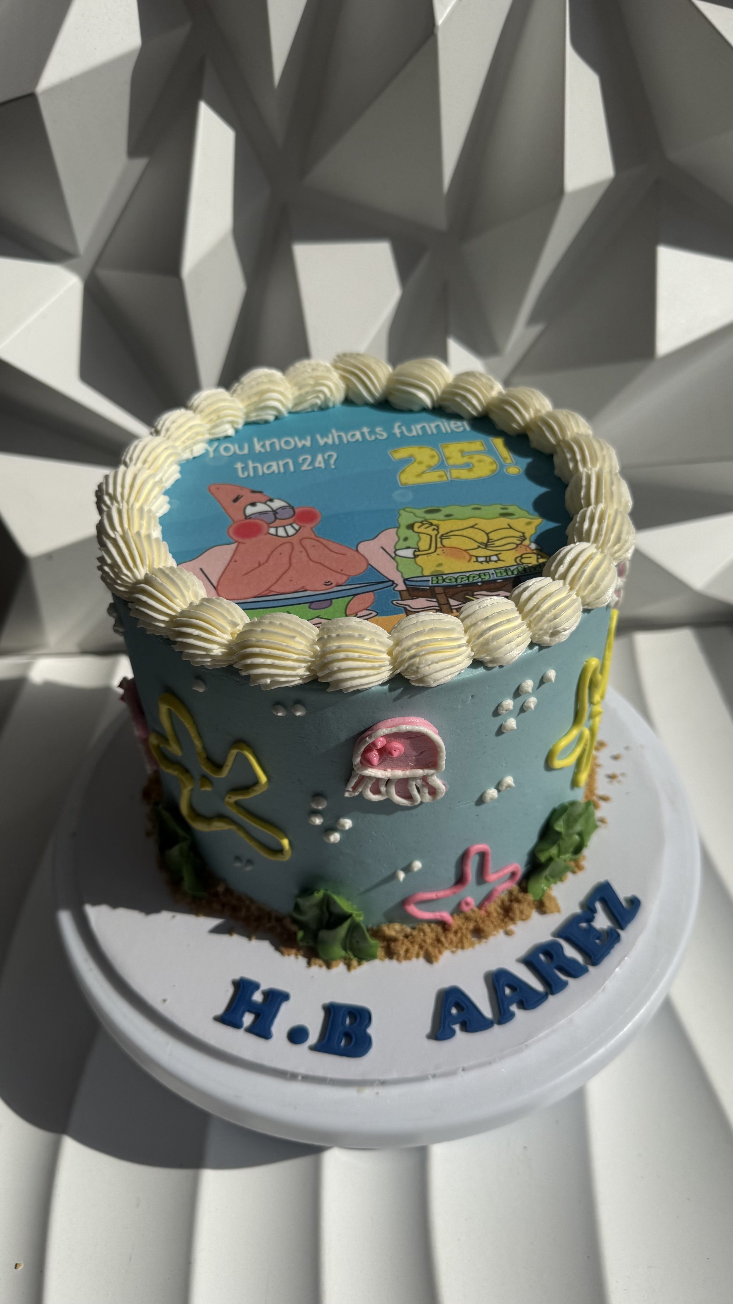 Pastel azul con decoraciones de personajes de dibujos animados, incluyendo Patricio y Bob Esponja, con un mensaje de cumpleaños y el nombre en la base del pastel.