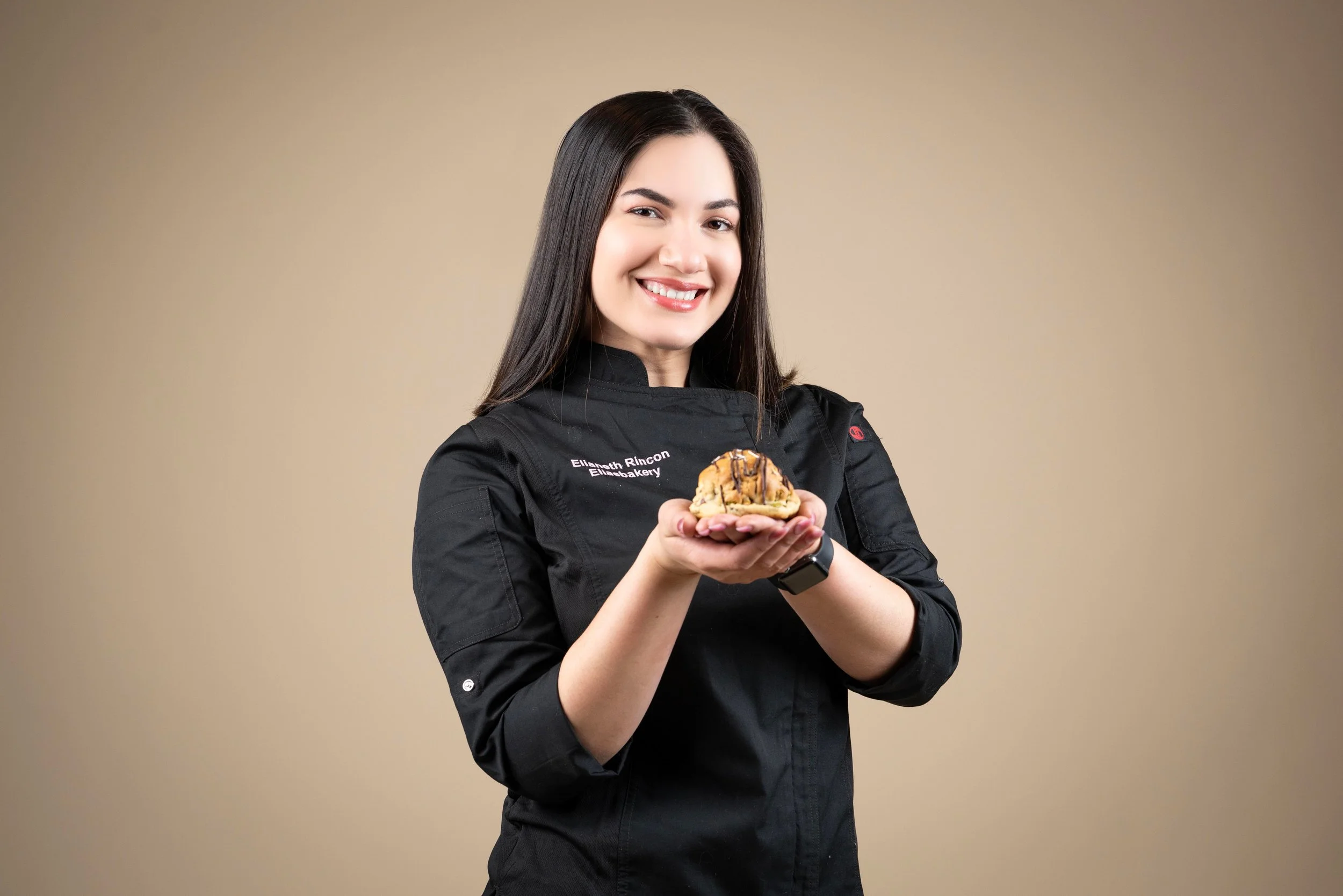 Mujer chef sonriendo y mostrando una cookie con chispas de chocolate y caramelo.