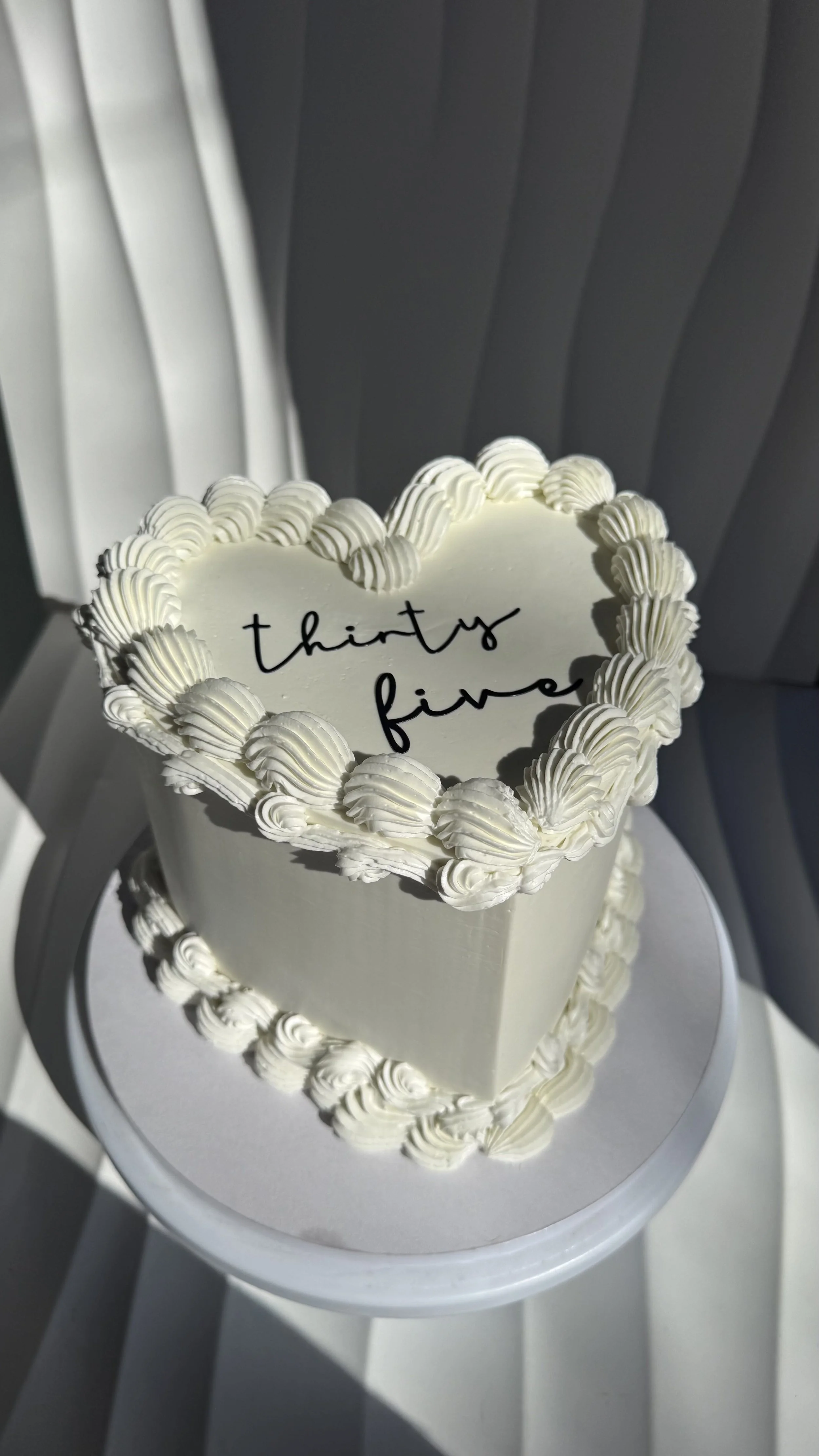 Pastel de pastel de boda con forma de corazón decorado con glaseado blanco y letras negras que dicen 'thirty five' en el centro.