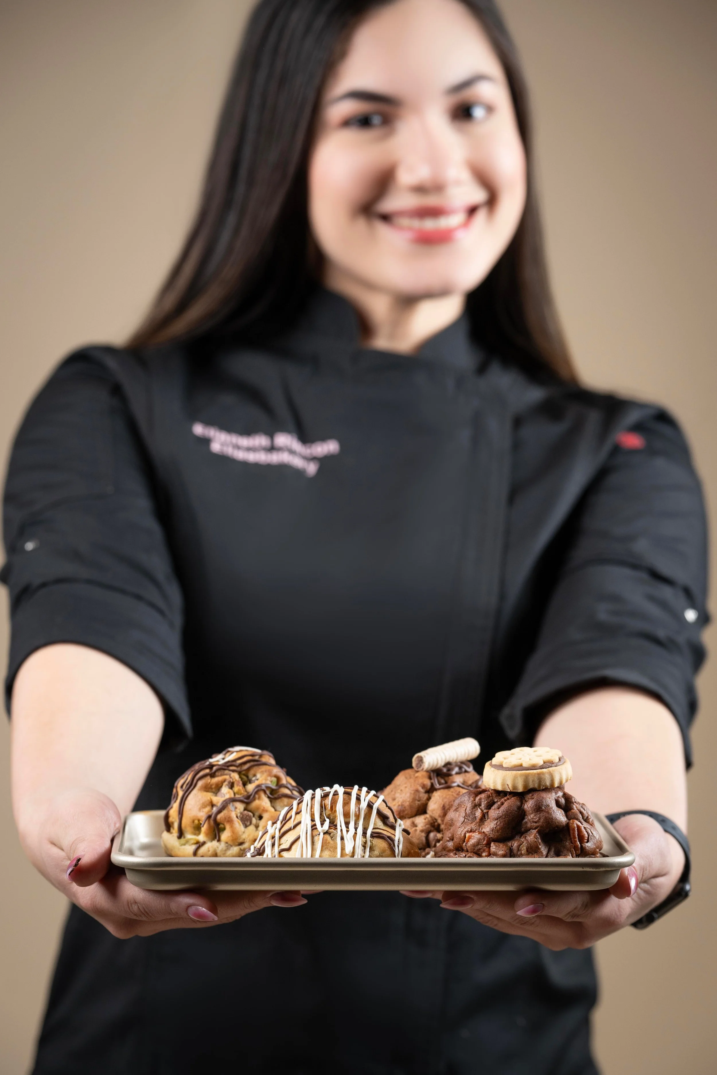 Mujer sosteniendo una bandeja con variedad de galletas decoradas con chocolate y chocolates.