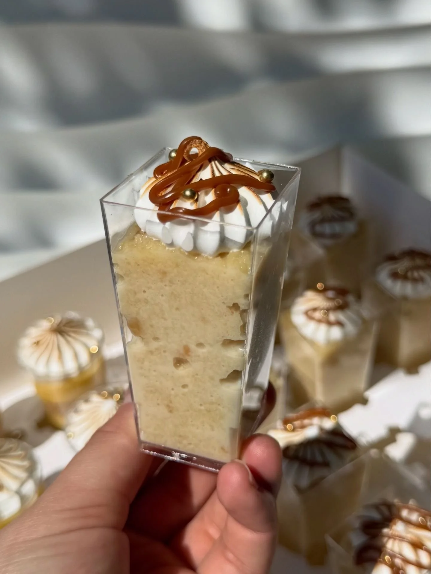 Un vaso con postre de vainilla con crema, decorado con dulce de caramelo y pequeñas perlas doradas.