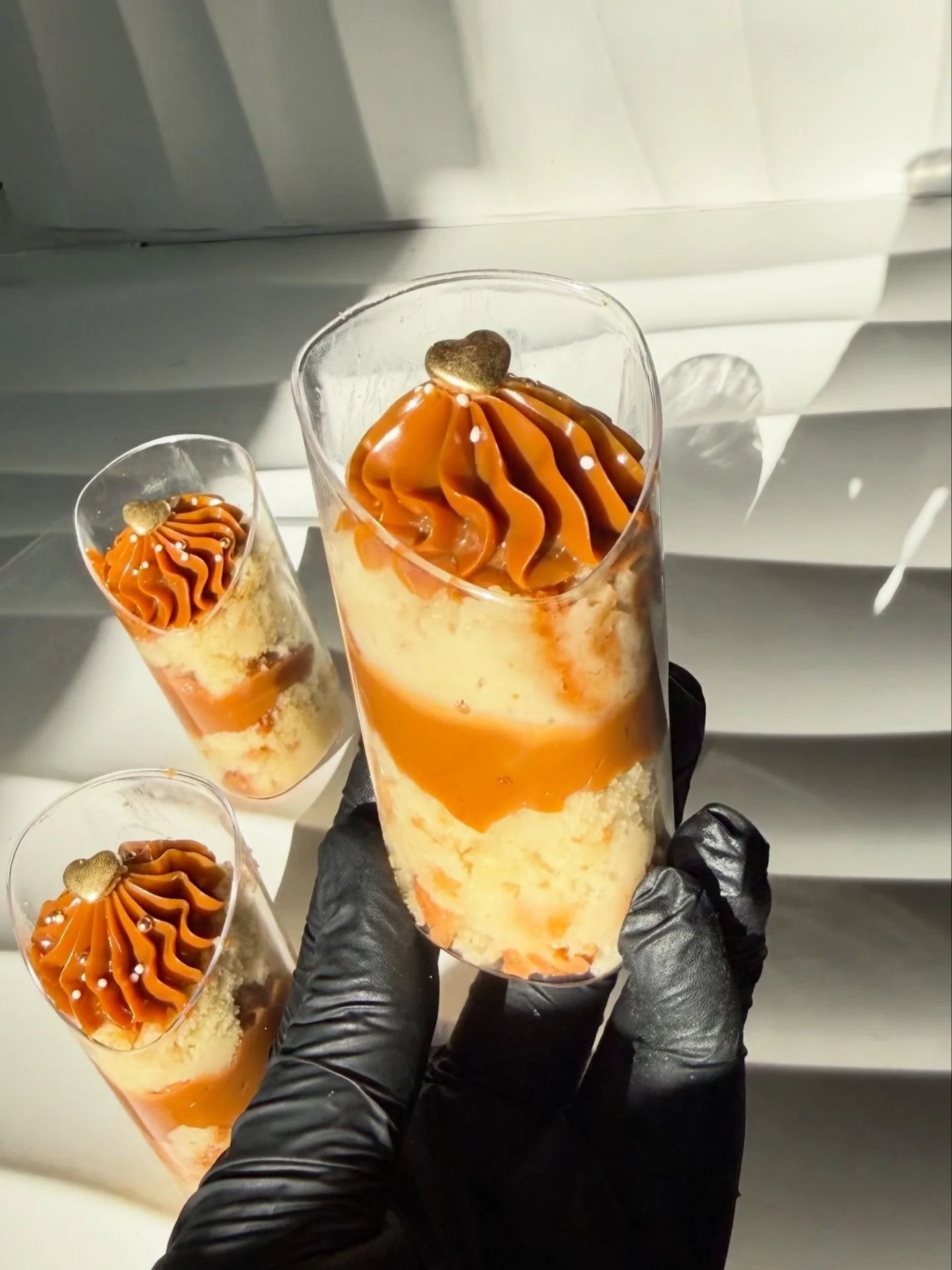 Vasos con postre de crema amarilla, caramelo en la parte superior y decoraciones blancas y doradas