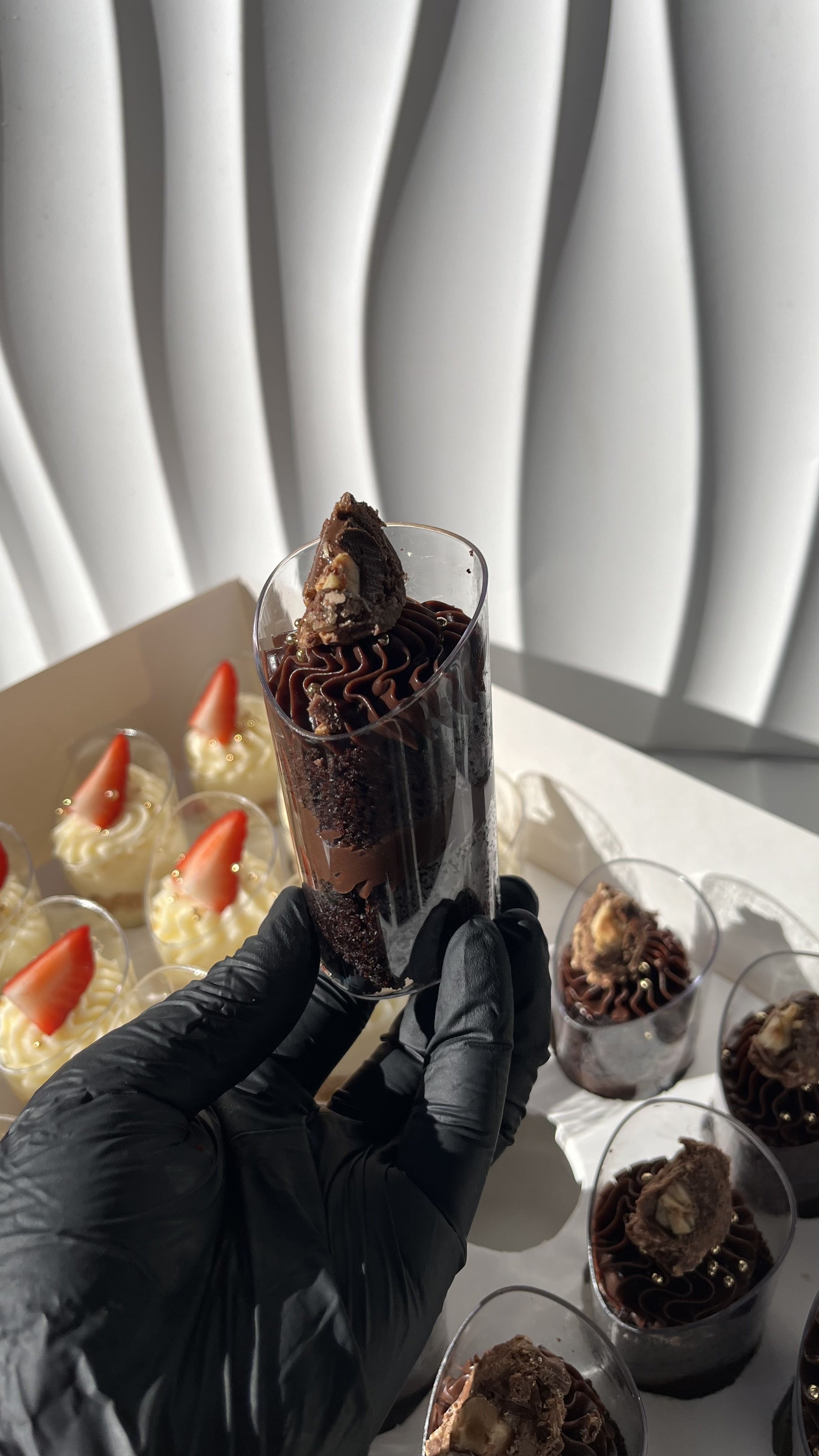 Vaso con postre de chocolate y trozo de chocolate en la parte superior, rodeado de otros postres con fresas.