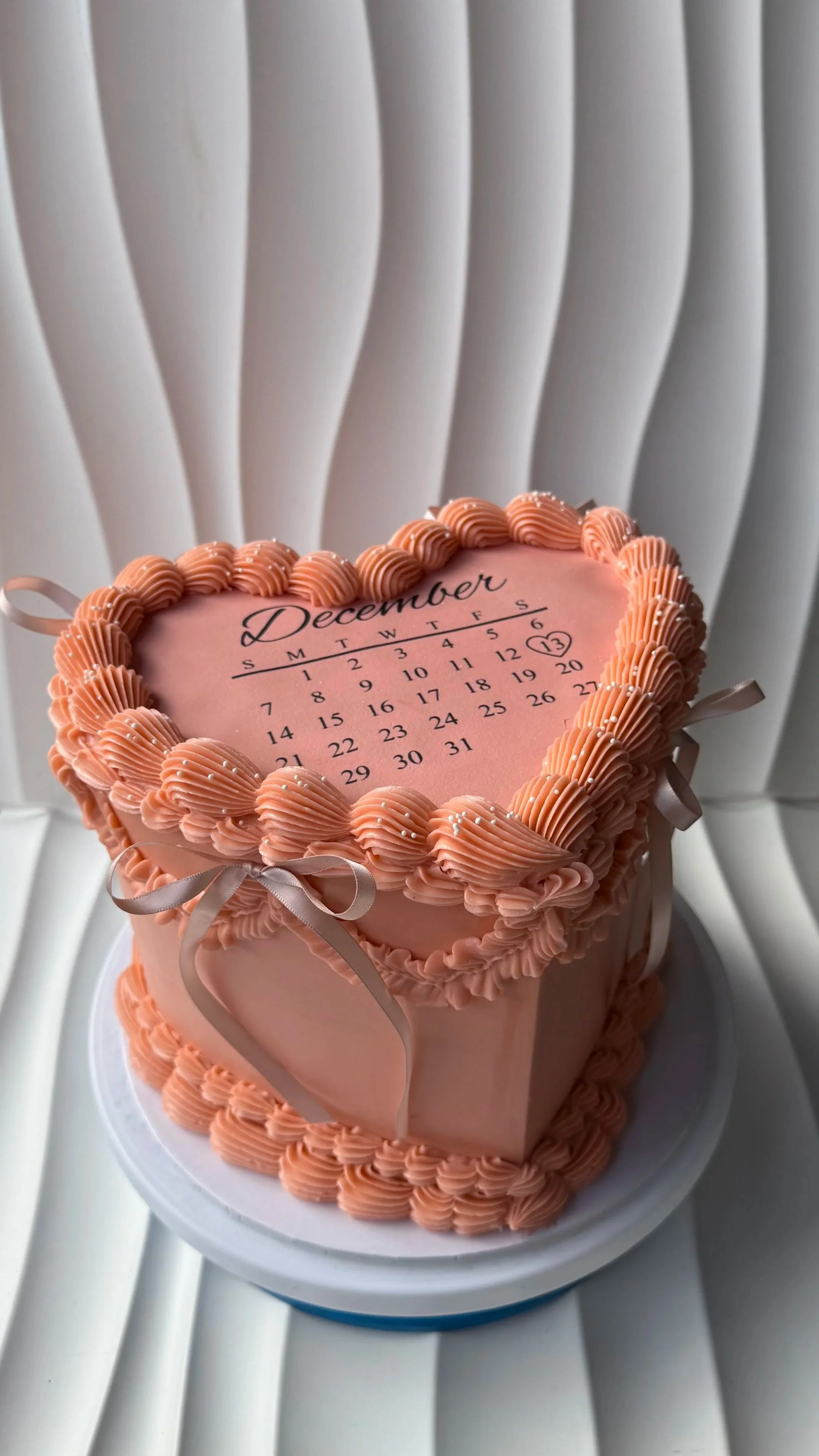 Pastel en forma de corazón con decoración rosa y calendario de diciembre en la parte superior, con el símbolo de un corazón y el número 13 resaltados.