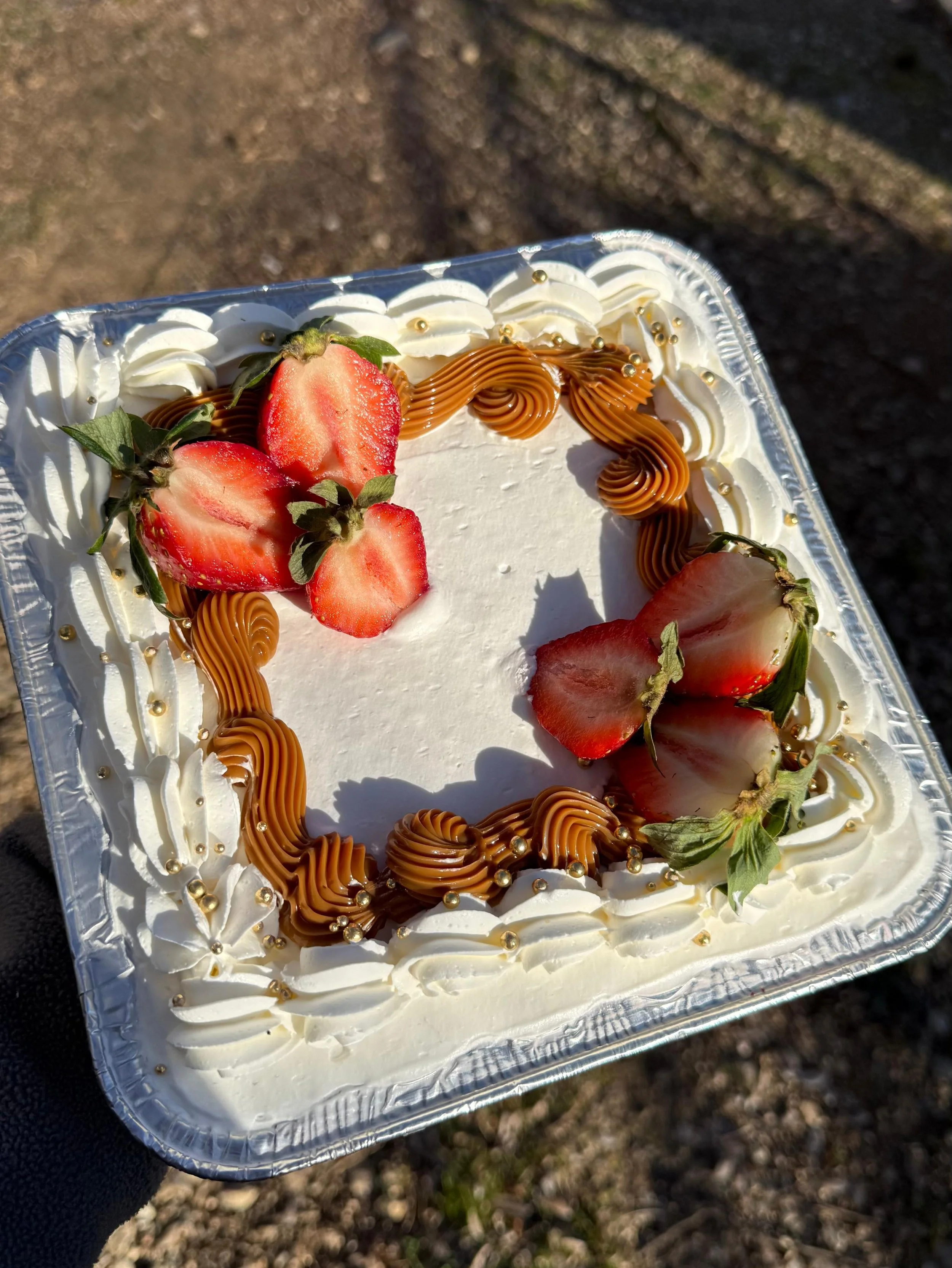 Pastel de fresas con crema, decorado con trozos de fresa y remolino de caramelo de chocolate en un recipiente de aluminio.
