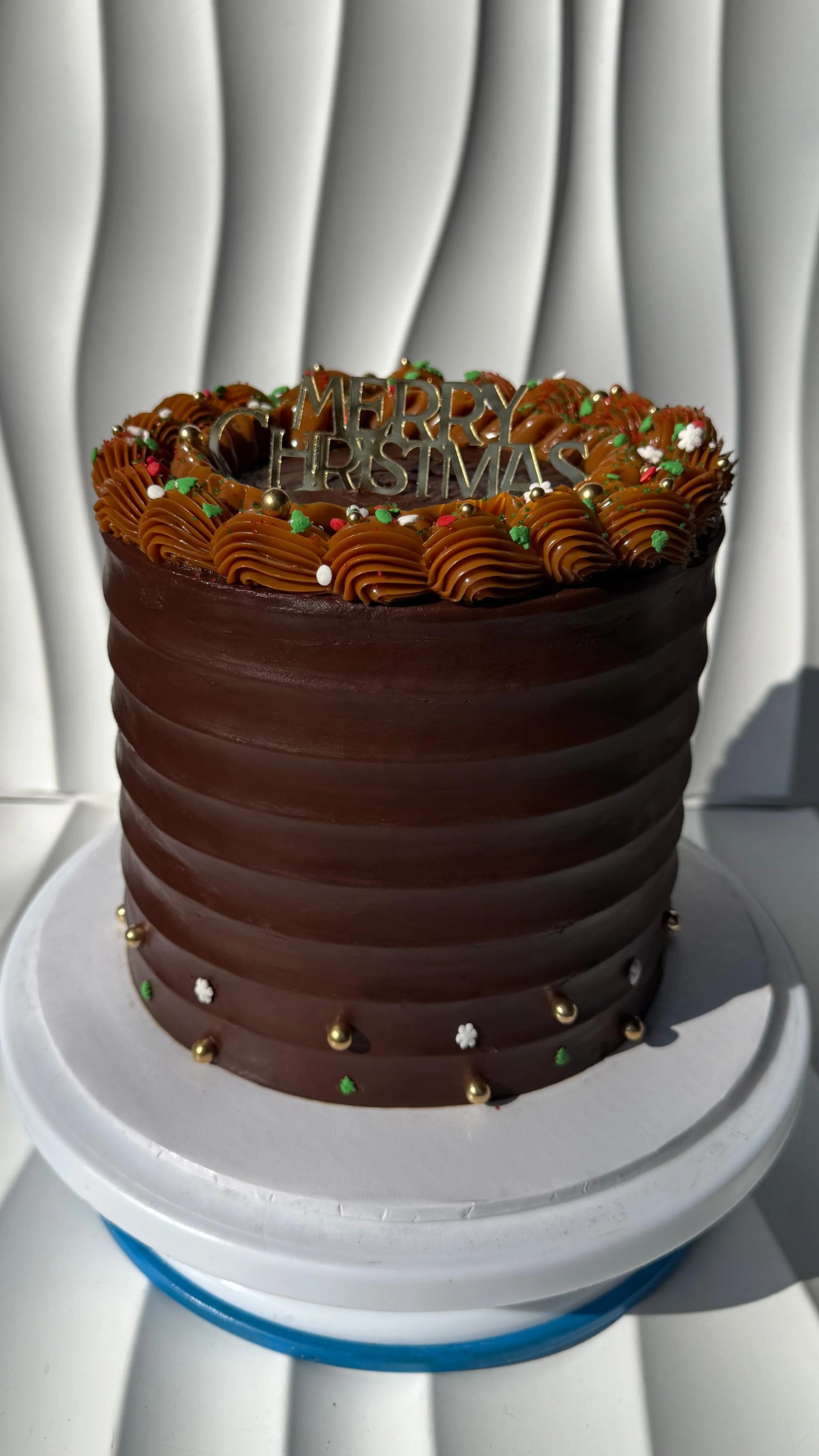 Pastel de chocolate decorado con un adorno que dice 'MERRY XMAS' y glaseado de chocolate con chispas decorativas.