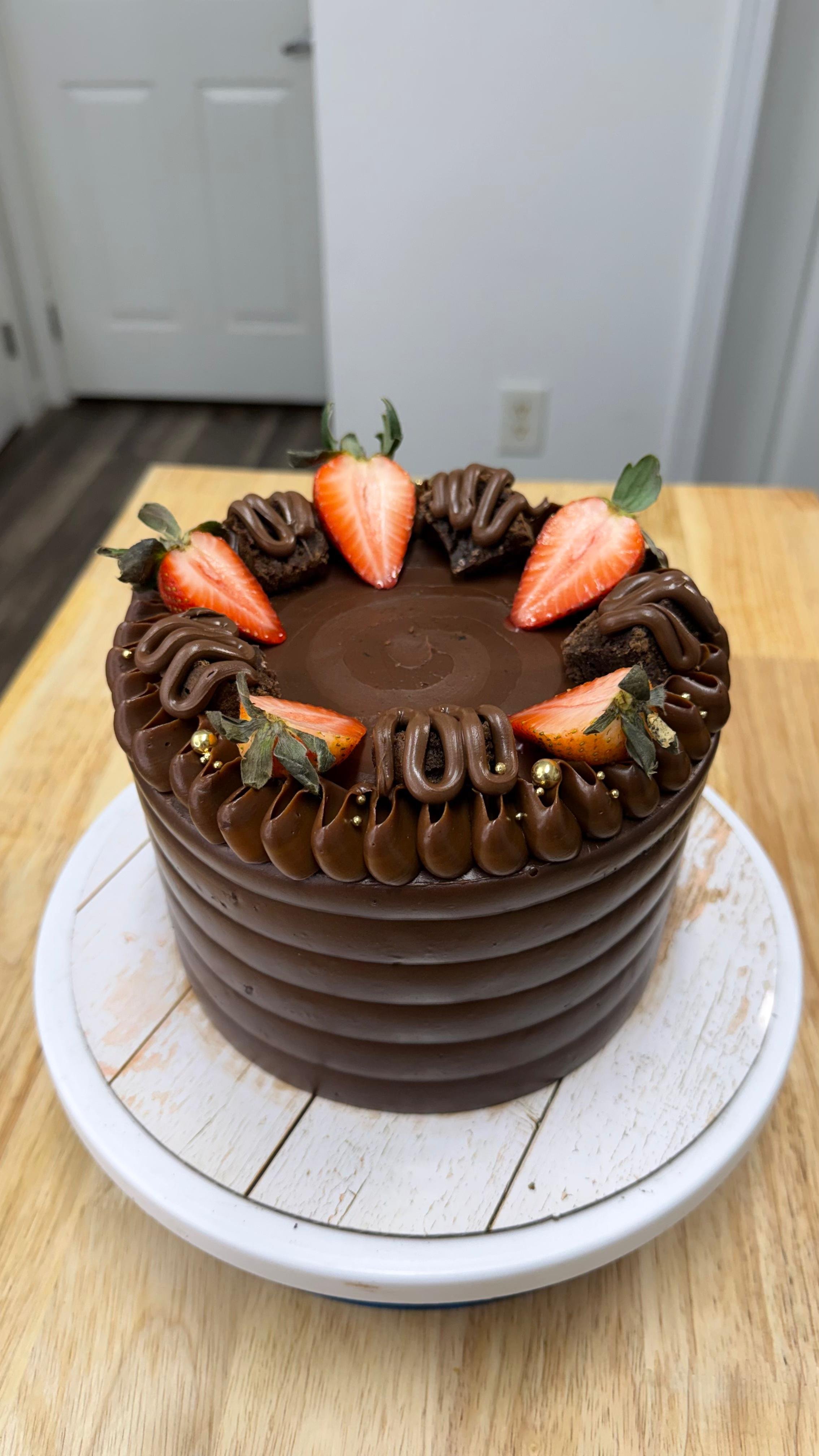 pastel de chocolate decorado con fresas, chocolate y pequeñas bolas doradas, sobre una mesa de madera