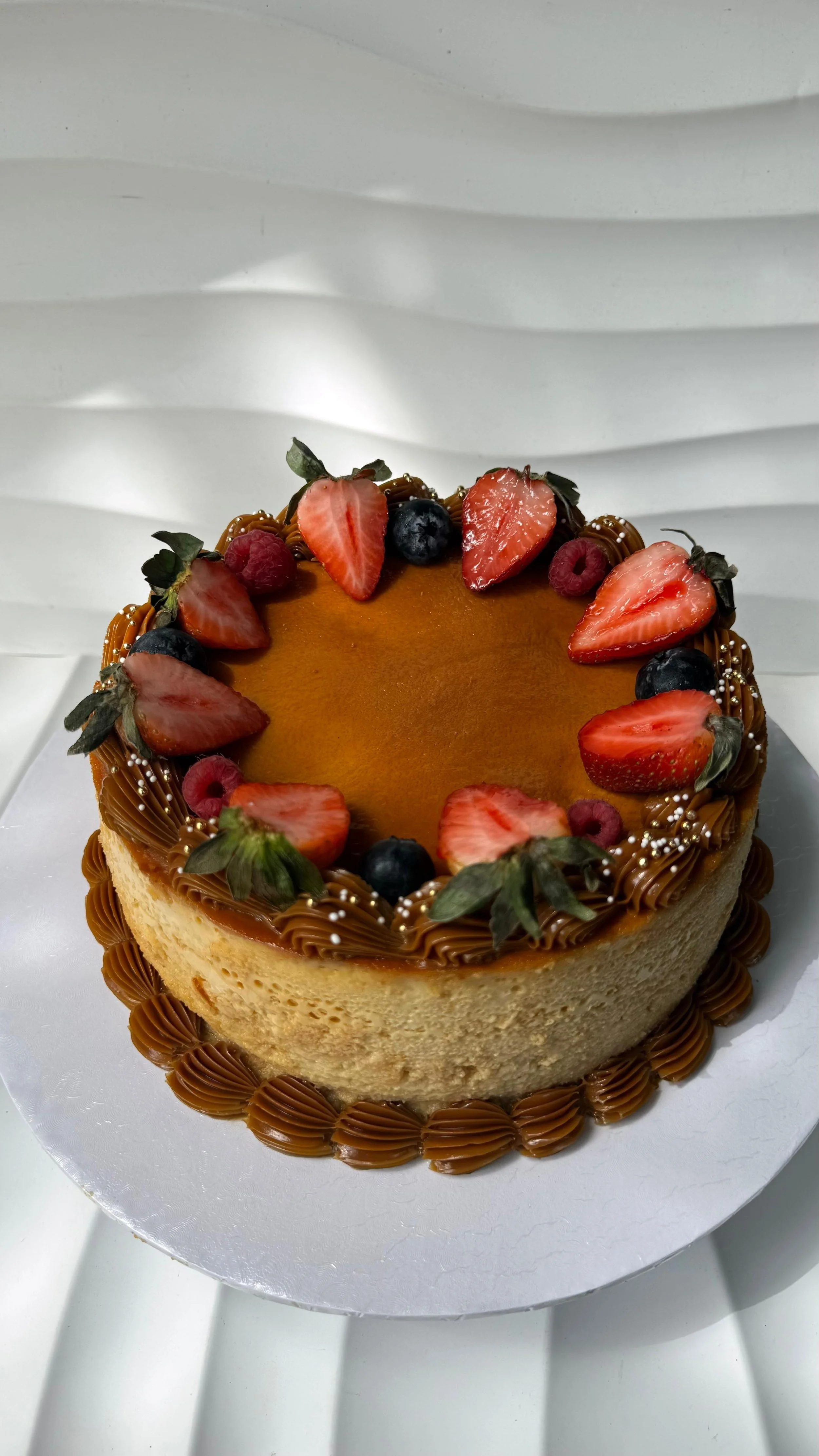 Pastel de cumpleaños decorado con fresas, moras, frambuesas, y pequeños topper dorados, con borde de betún de chocolate y base de cartón.