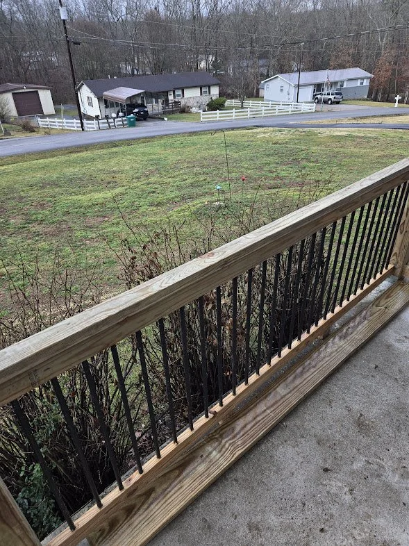 View from a wooden balcony overlooking a grassy yard with trees in the background and neighboring houses.