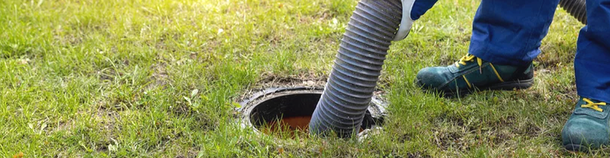 Person using a hose to clear a drain in the grass.