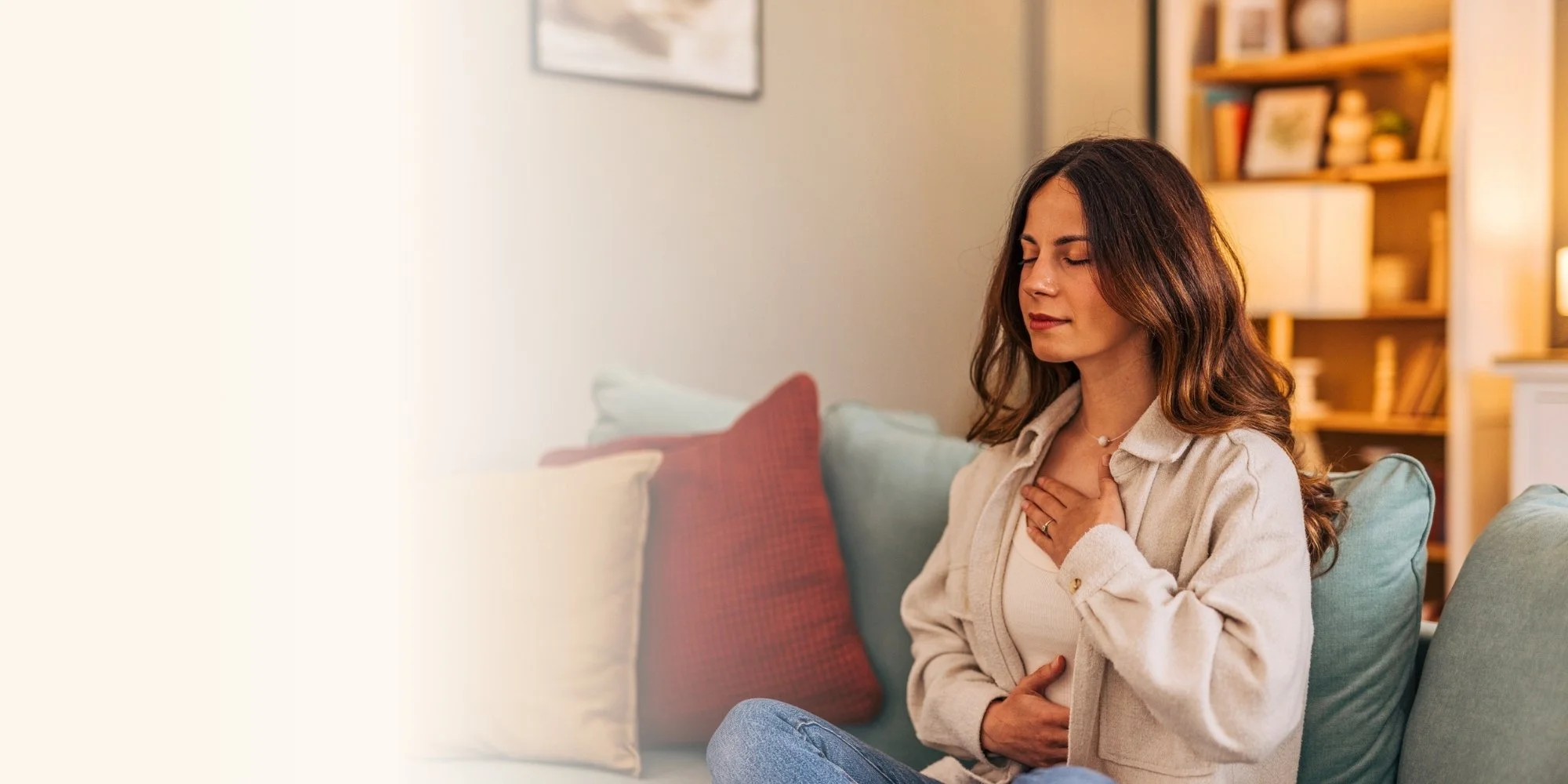 A woman sitting on a couch, holding her chest with a concerned expression, indicating she may be experiencing chest pain or discomfort in a cozy living room setting.