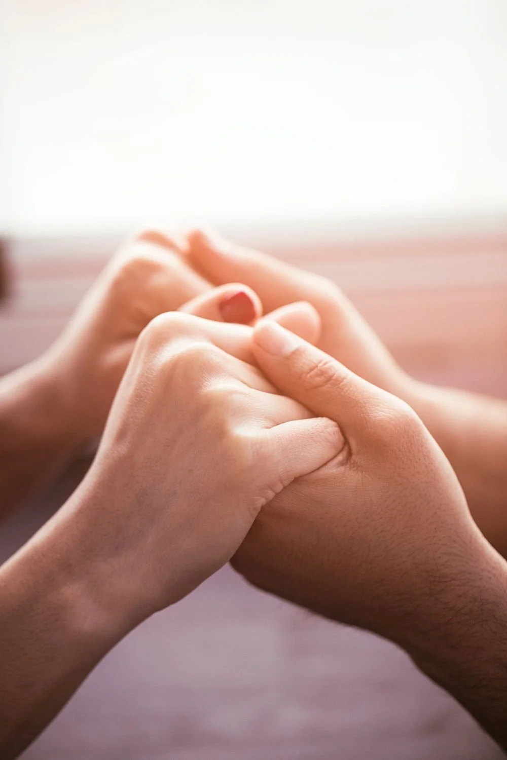 Two pairs of hands, one light-skinned and one dark-skinned, gently holding each other's fingers in a comforting gesture.