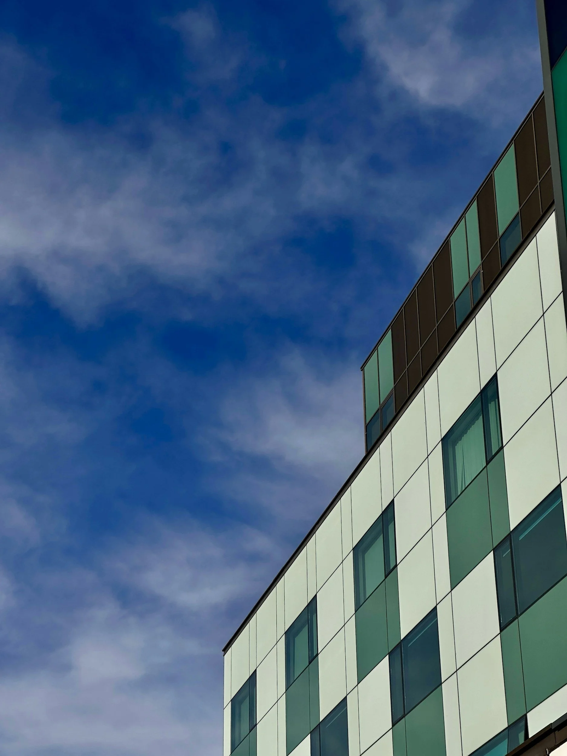 Close-up of a modern glass building with reflective windows against a clear blue sky with some clouds.