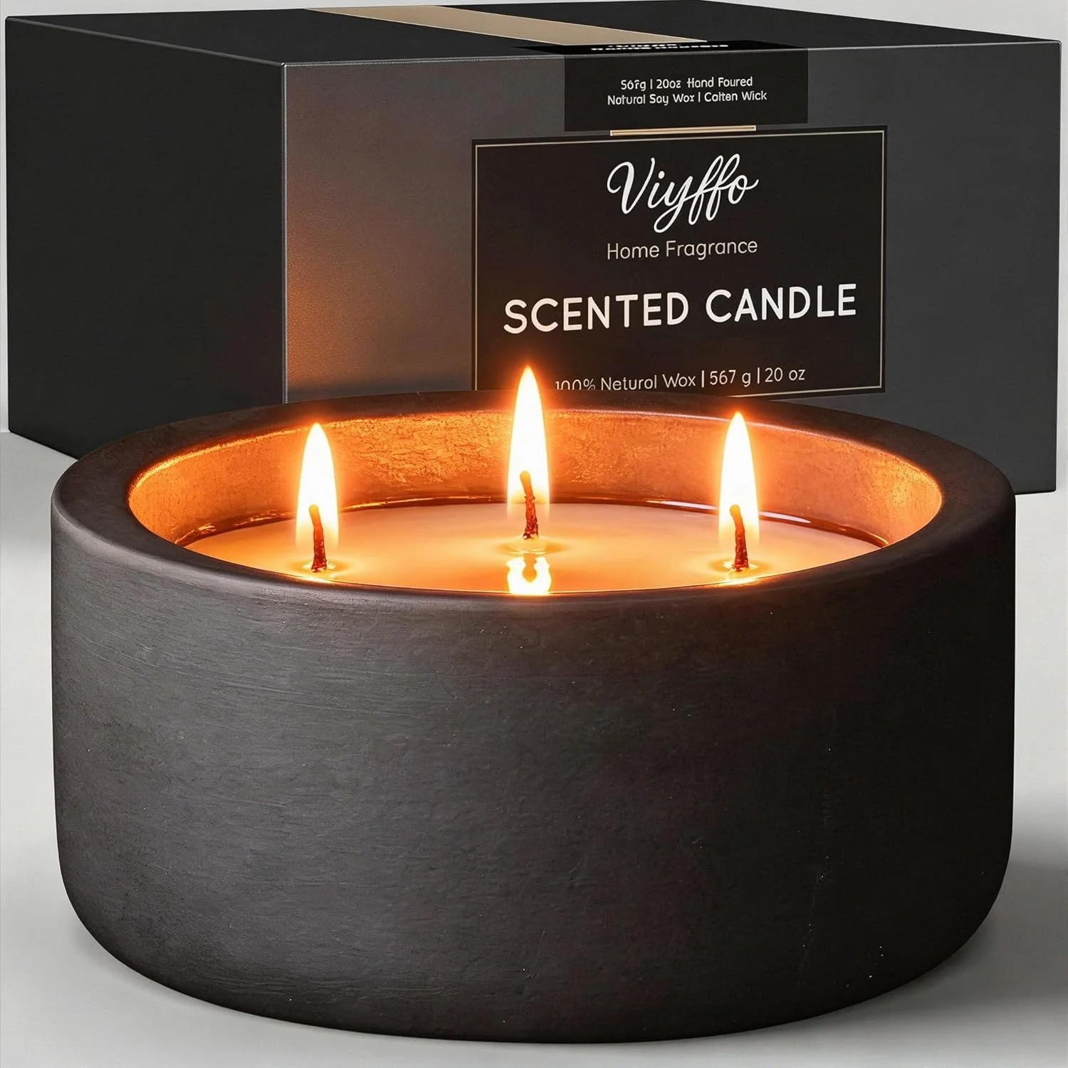 Black scented candle with three flames in a round holder, with packaging in the background.