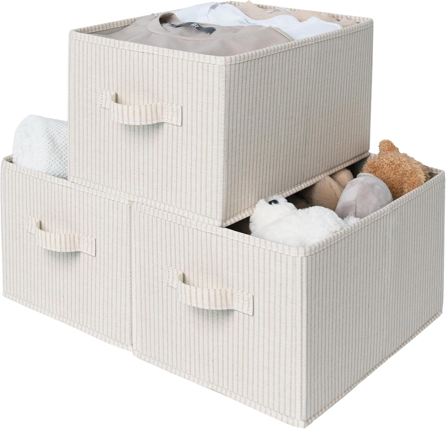 Two fabric storage boxes with handles, stacked. The bottom box contains stuffed animals, including a white fluffy one, a grey animal, and a brown teddy bear. The top box has some clothing items inside.