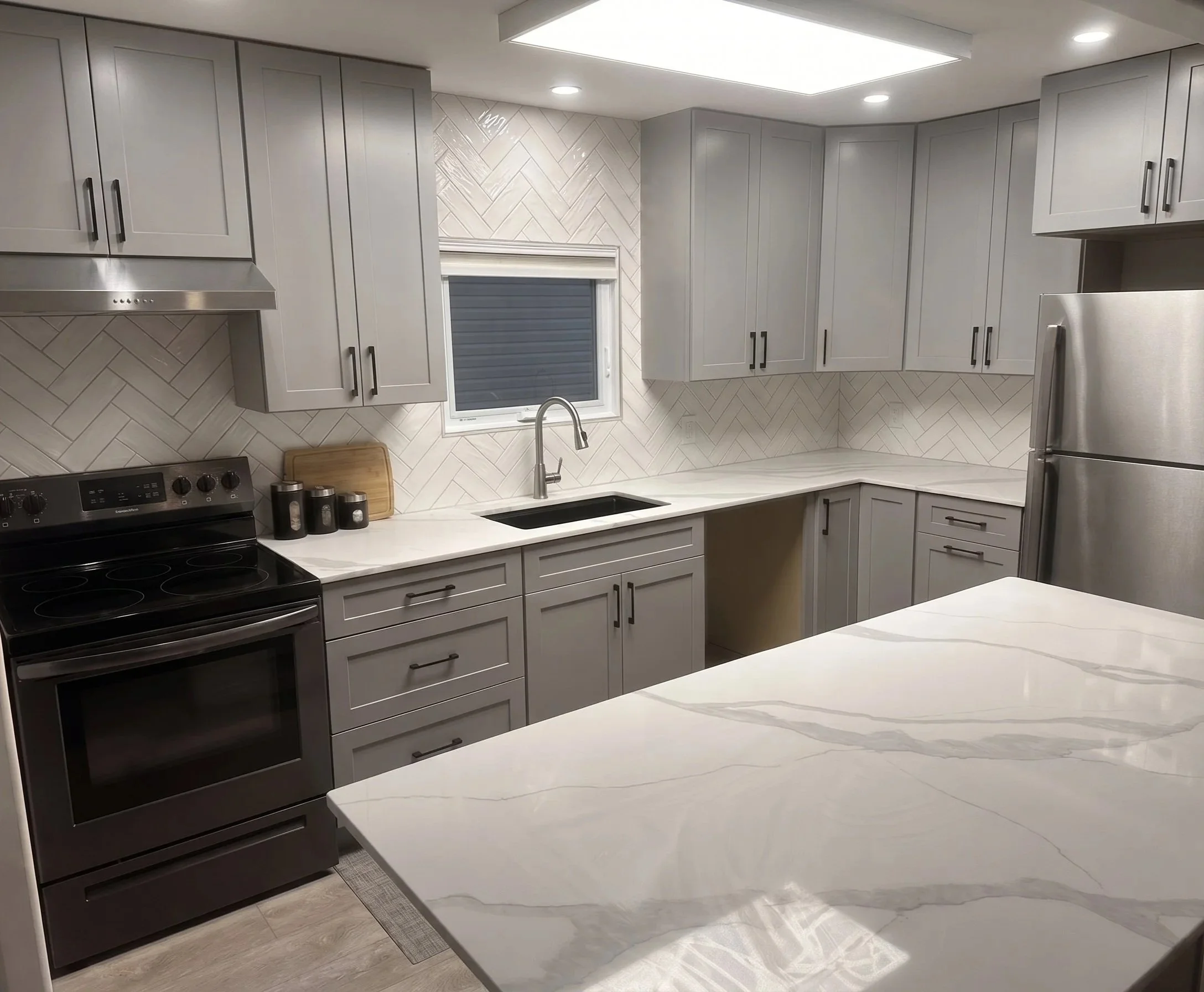 A modern white kitchen with stainless steel appliances, including a refrigerator, oven, and microwave, and a marble backsplash.