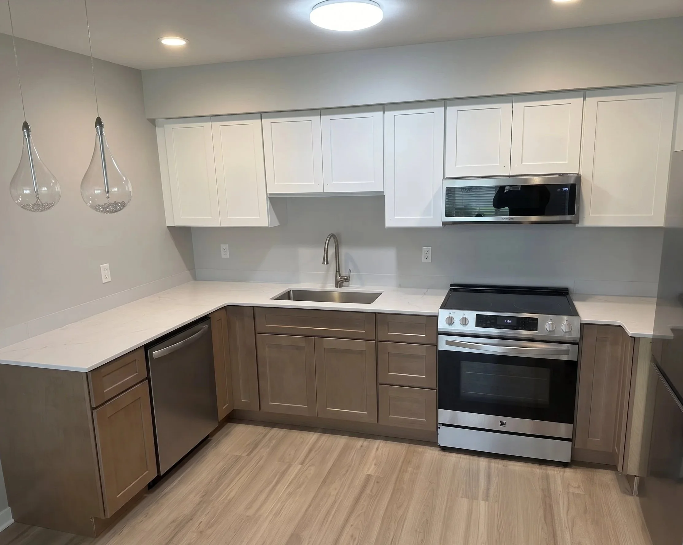 kitchen renovation with real projectsKitchen with grey cabinets, a window, a white dishwasher, and a white stove with coil burners. The cabinets are being installed or renovated, and some cabinet doors are missing. There is a ladder on the left side.