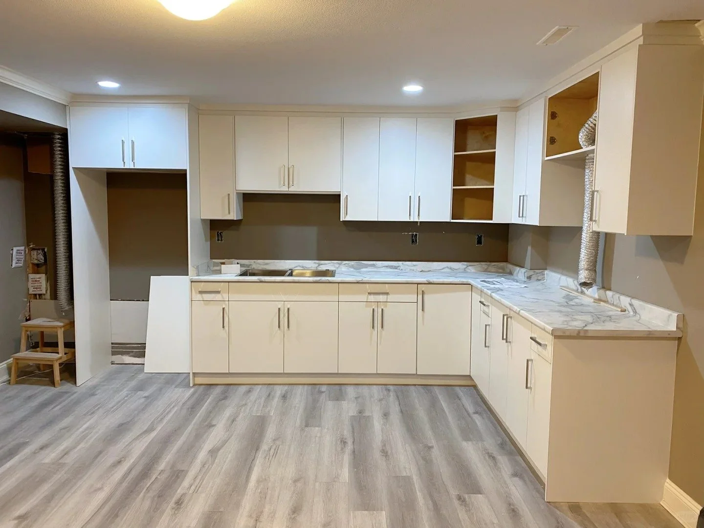 Unfinished kitchen with white cabinets, marble countertops, and a grayish wood floor, in a room with painted gray walls and no appliances installed.