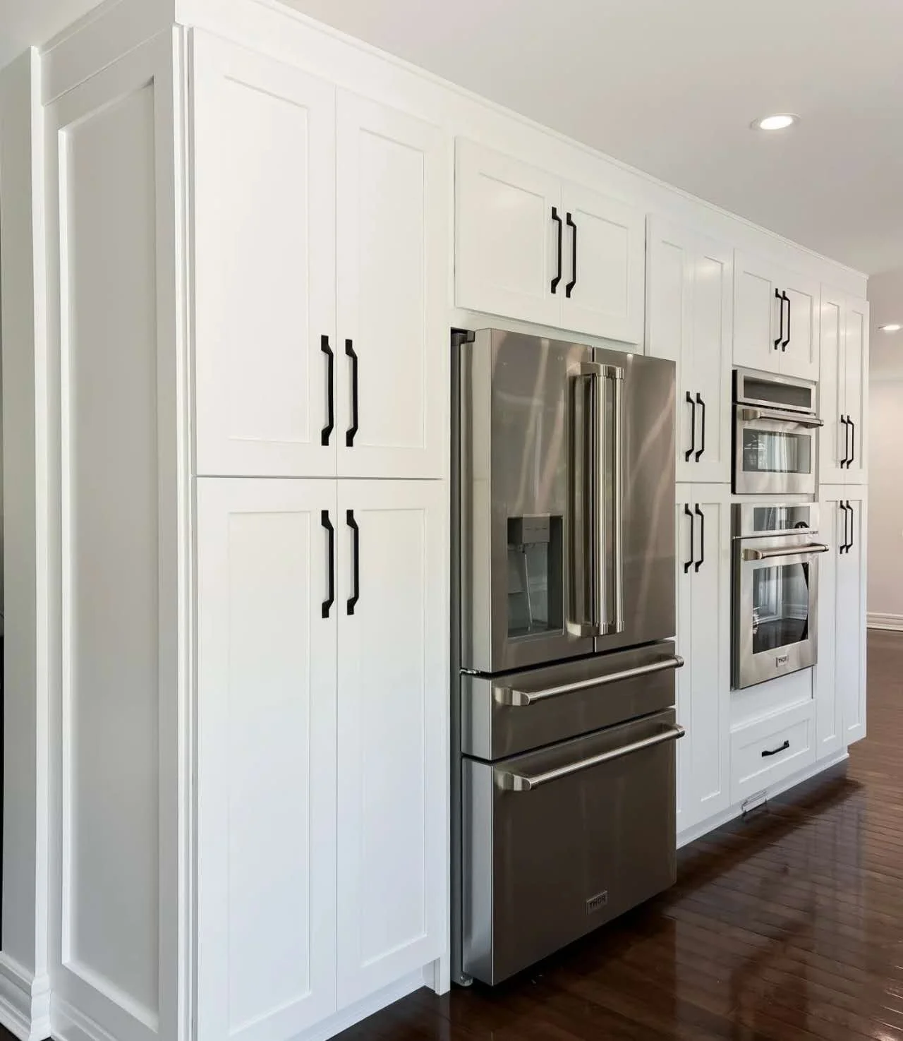 White kitchen cabinets with black handles and stainless steel refrigerator and oven built into the cabinetry.