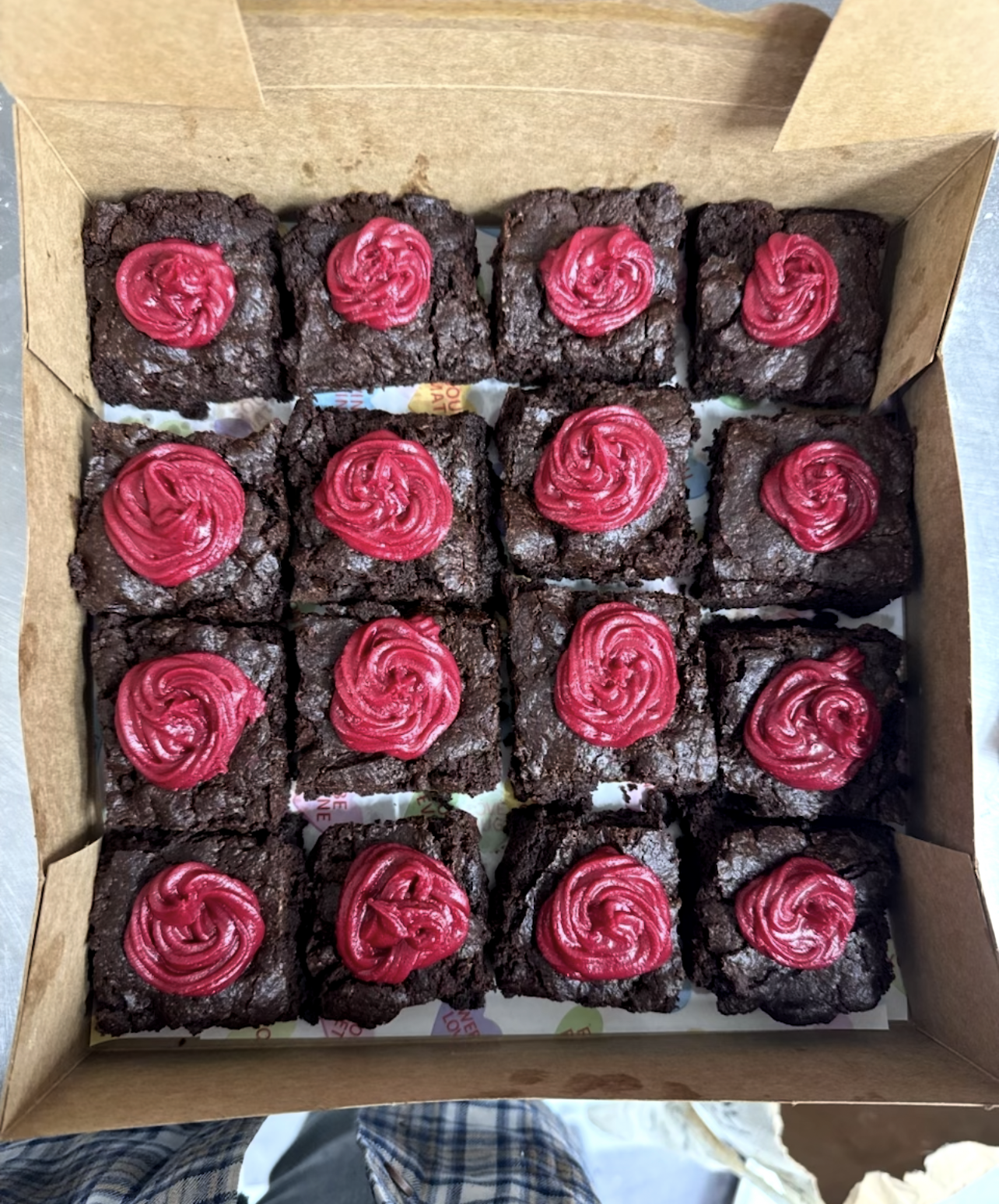 A box of twelve chocolate brownies topped with pink swirled icing.
