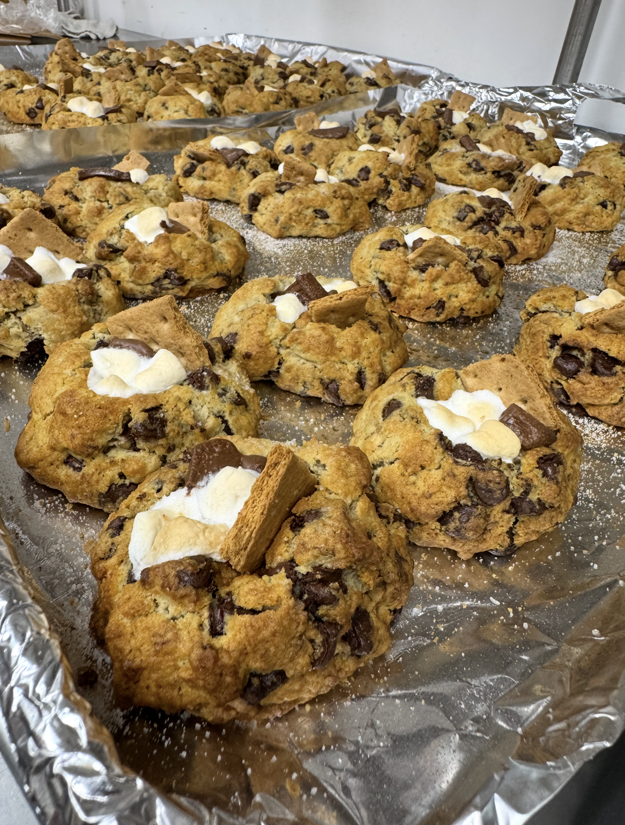 Freshly baked chocolate chip cookies topped with marshmallow and Oreo pieces on a baking sheet covered with aluminum foil.