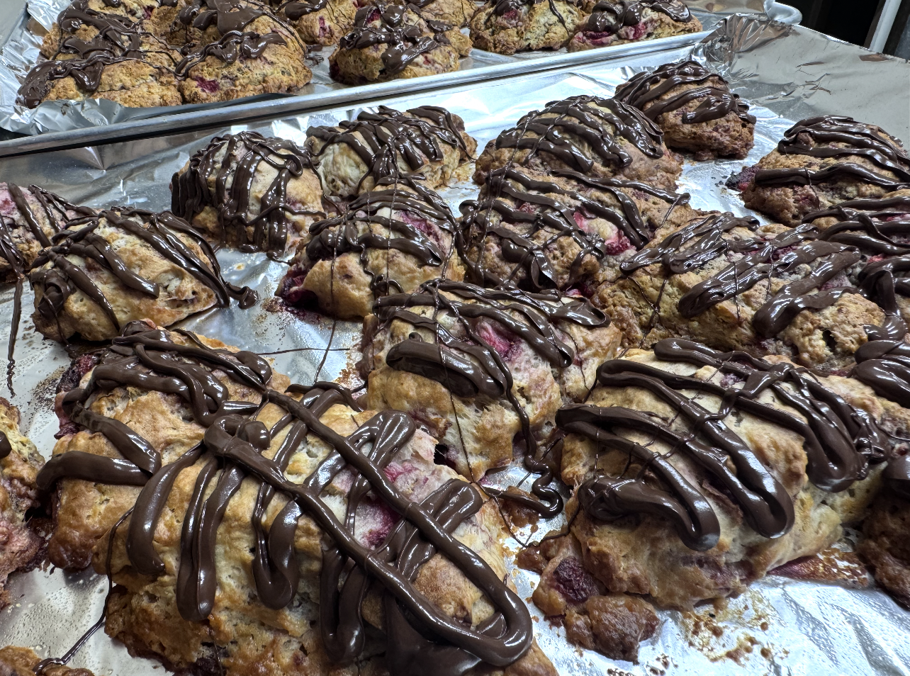 Freshly baked berry scones drizzled with chocolate, laid out on a baking sheet lined with aluminum foil.