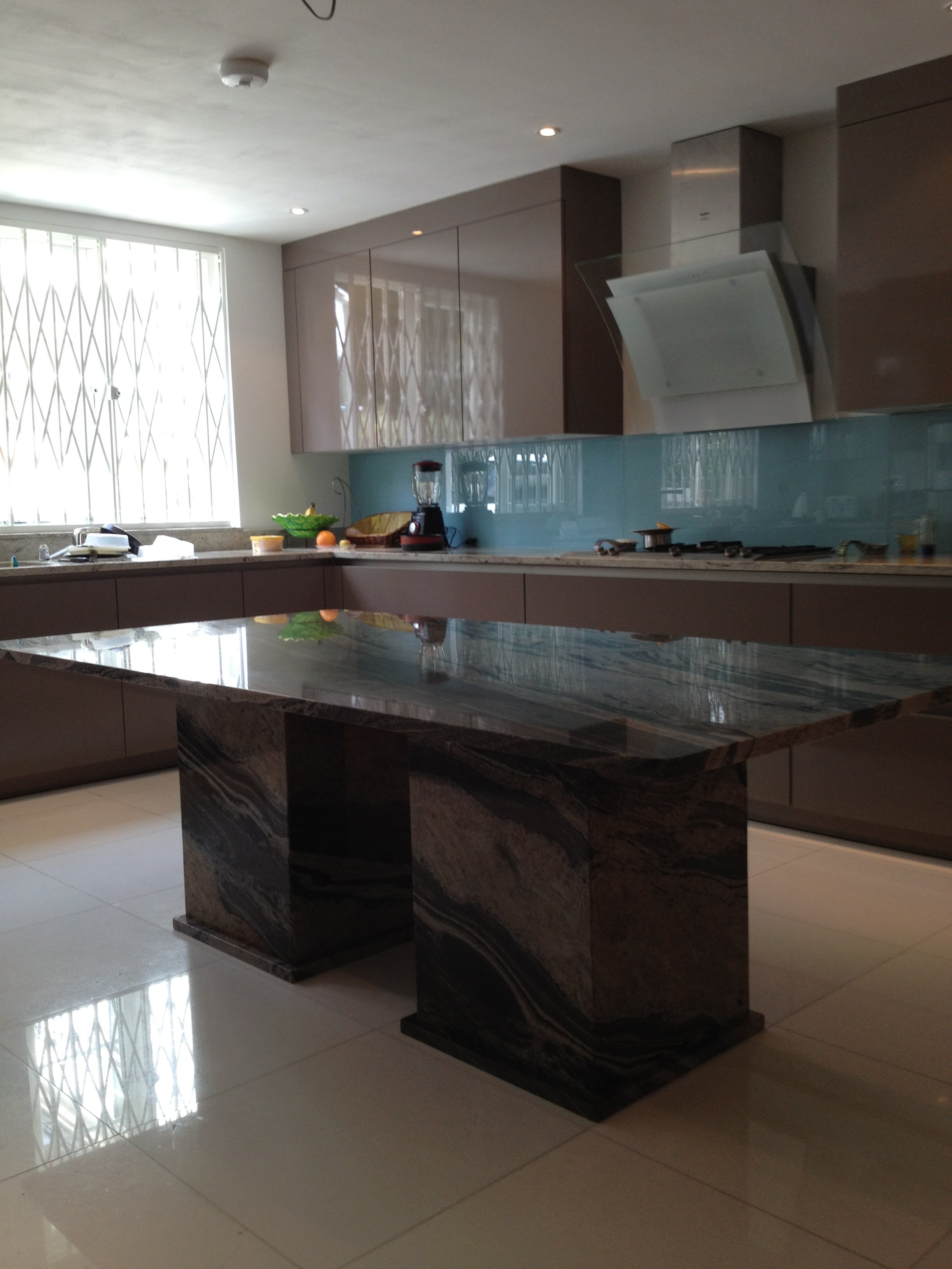 Modern kitchen with marble island, beige cabinets, glass backsplash, and tiled floor, with natural light coming through a window.