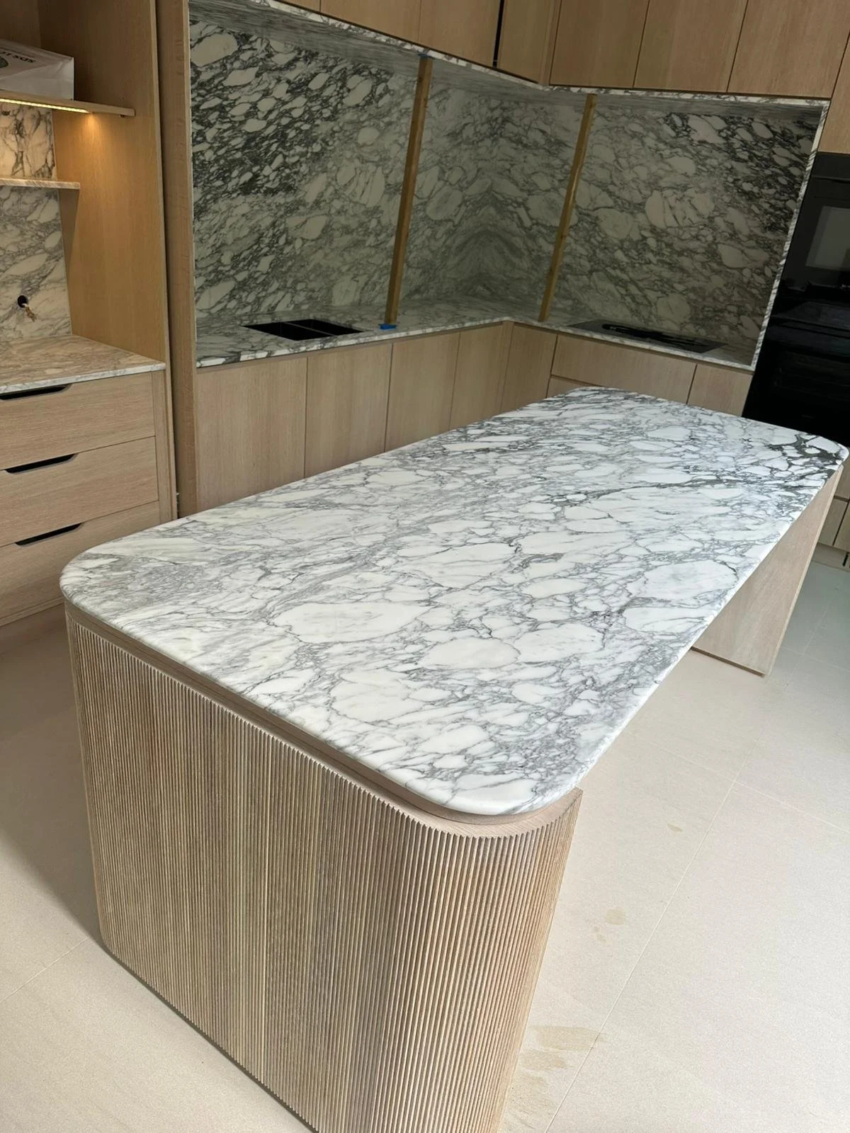 Kitchen island with a white marble countertop with gray veining and a curved, ribbed wood base.