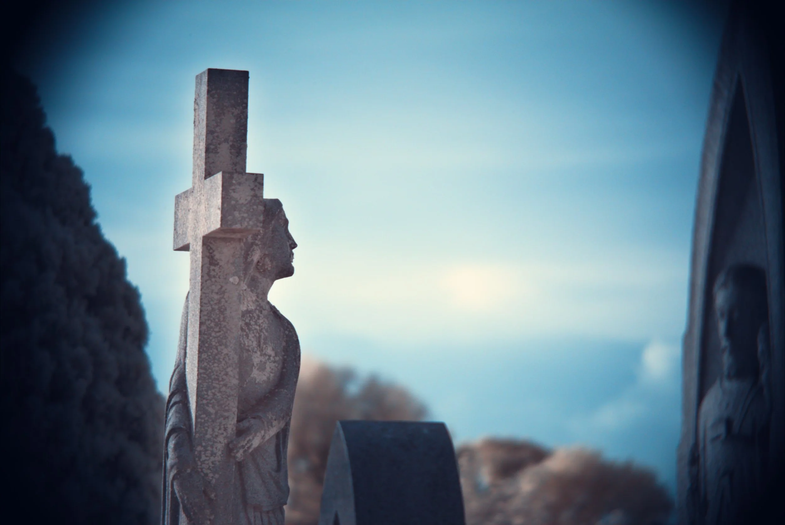 An infrared image of a gravestone portraying a man carrying a cross