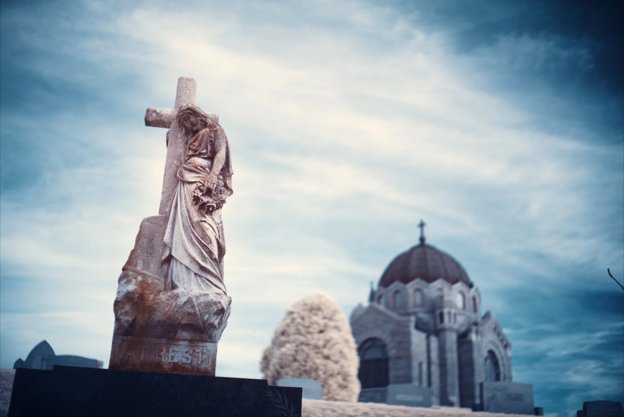 An infrared image of a gravestone portraying a man carrying a cross