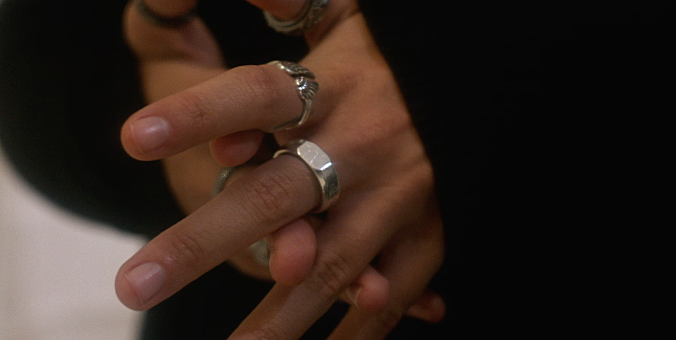 Multiple hands wearing silver rings, layered on top of each other, with a dark blurred background.