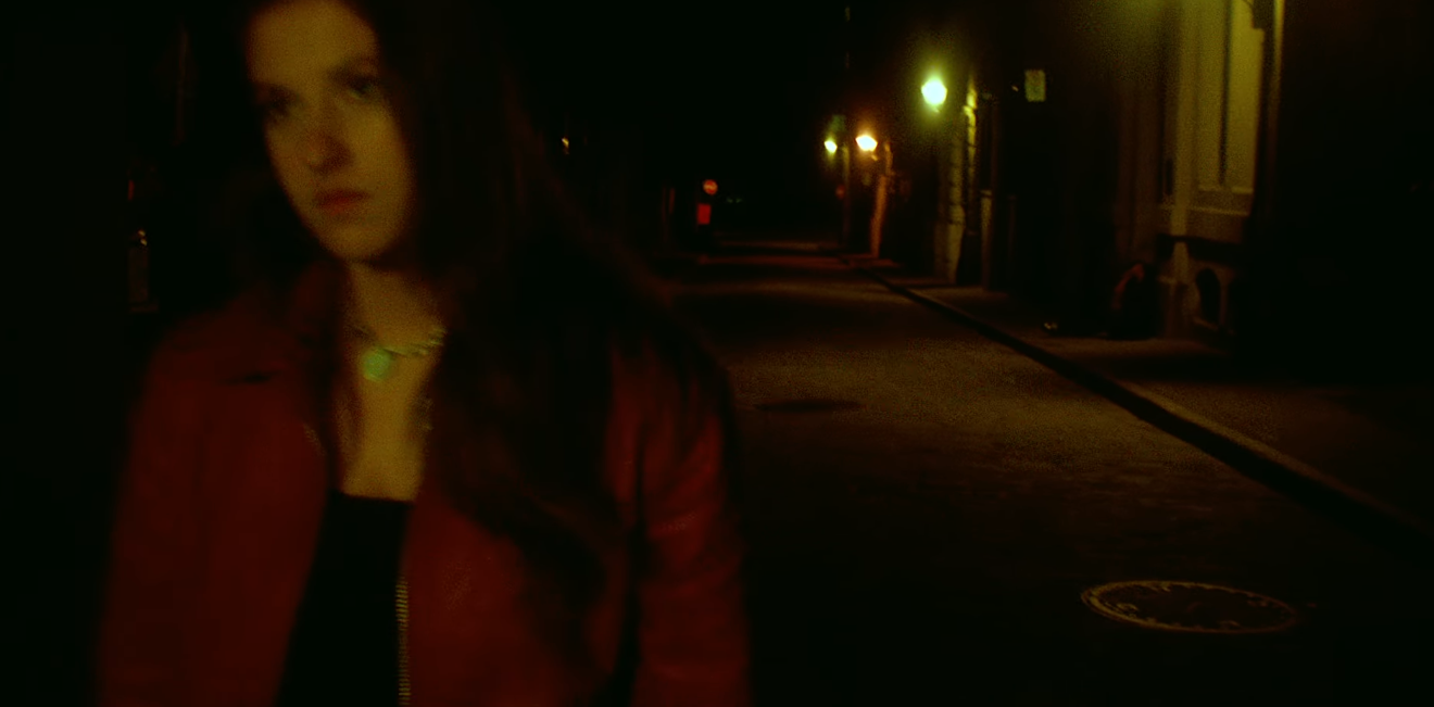 A woman with long dark hair wearing a red jacket standing on a dimly lit street at night