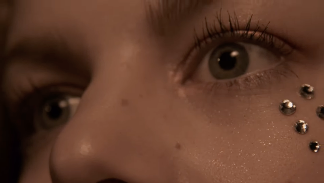 Close-up of a person's face with metallic gems near the right eye and sparkling makeup.