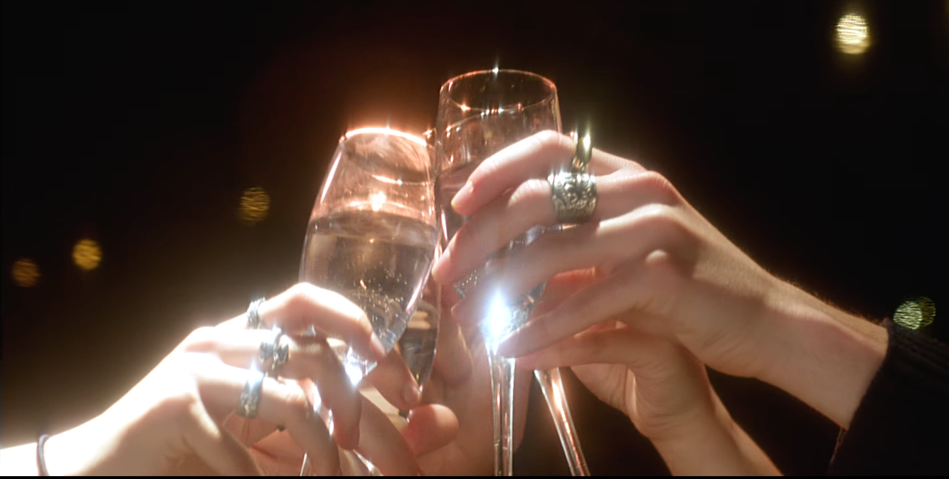 Four hands wearing rings are clinking champagne glasses filled with sparkling wine in a celebration setting.