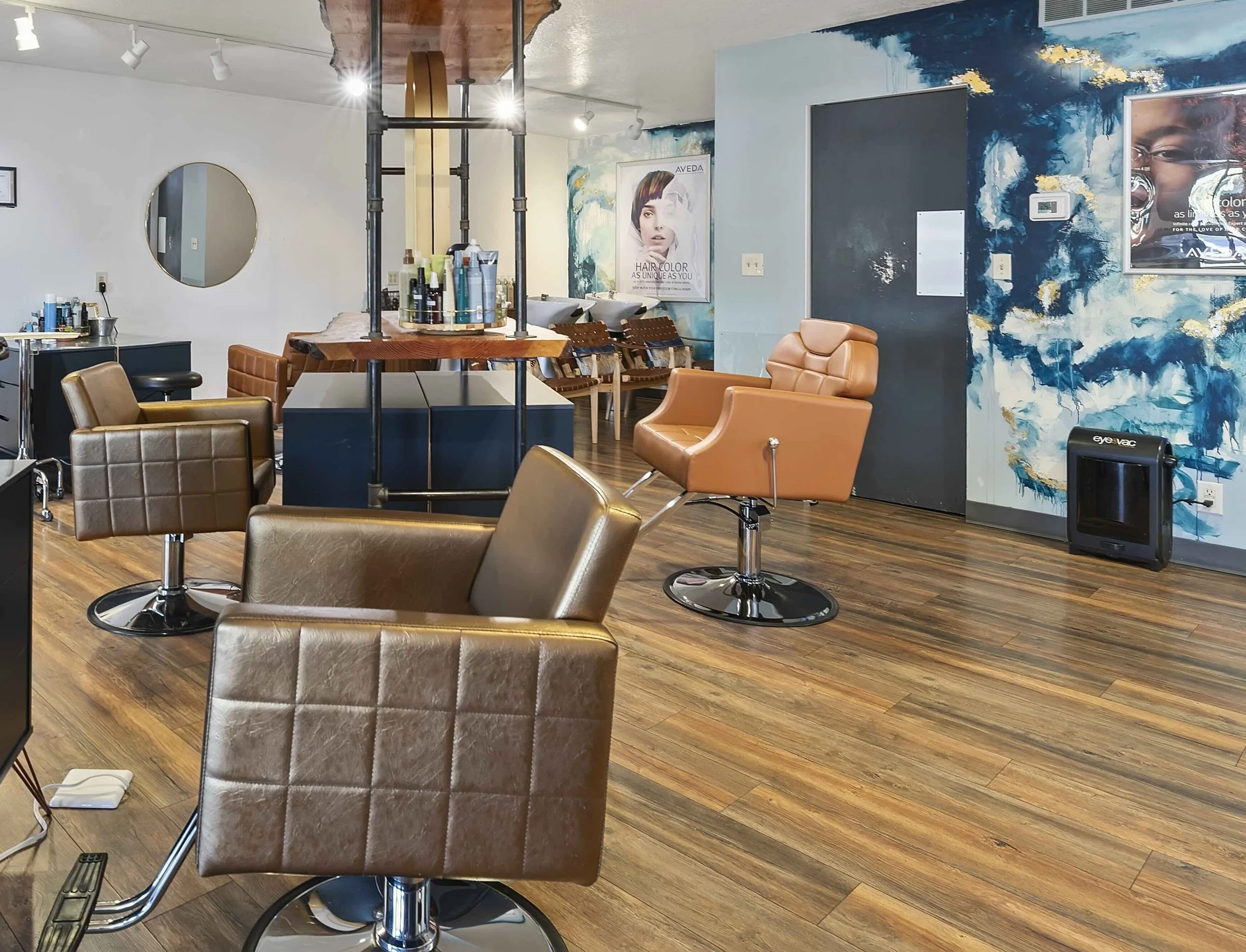 Interior of a hair salon with styling chairs, a wall mirror, posters, and hair treatment products.