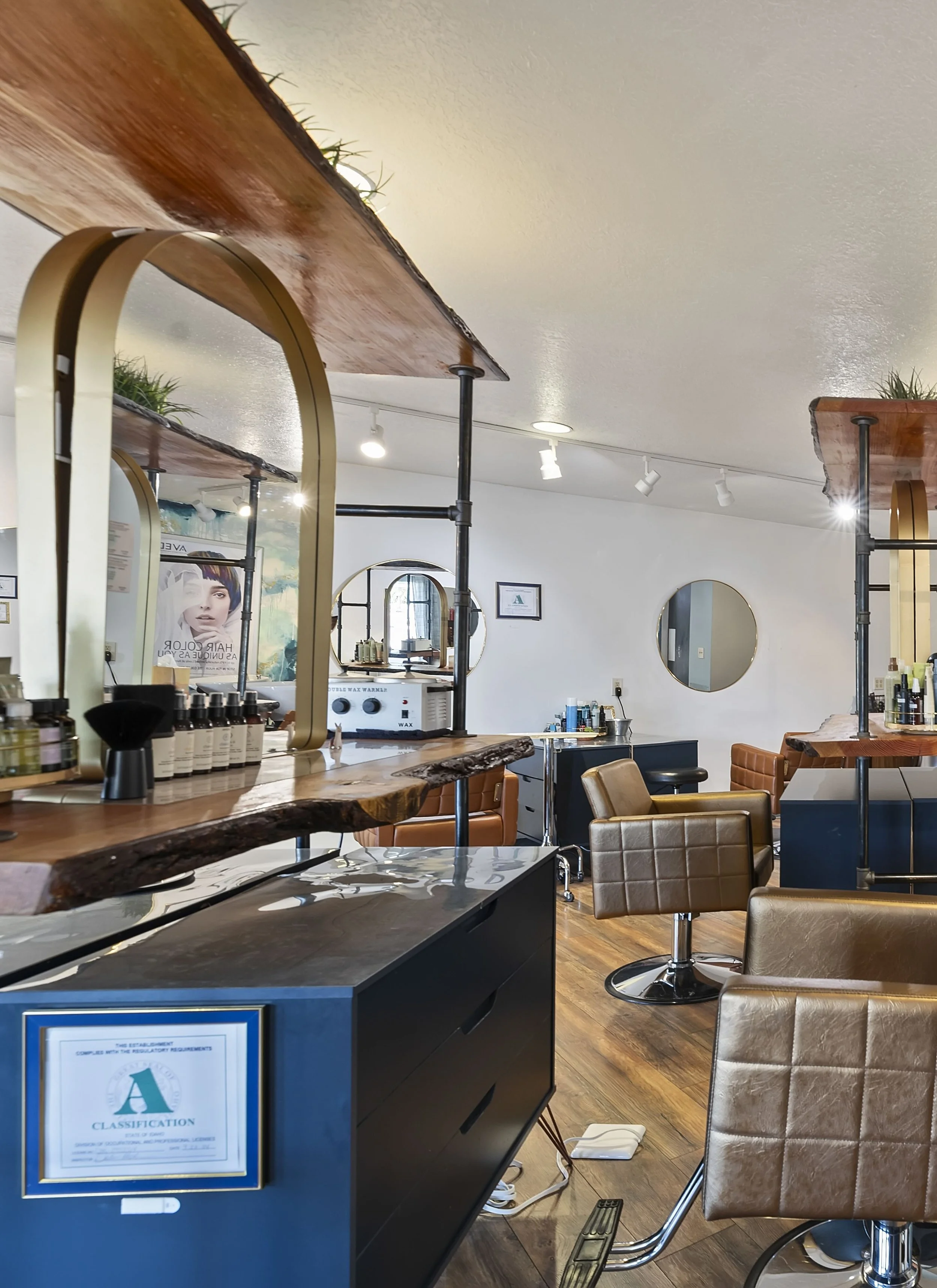 Interior of a hair salon with styling chairs, mirrors, and hair care products on a wooden counter, with track lighting and framed artwork on the wall.