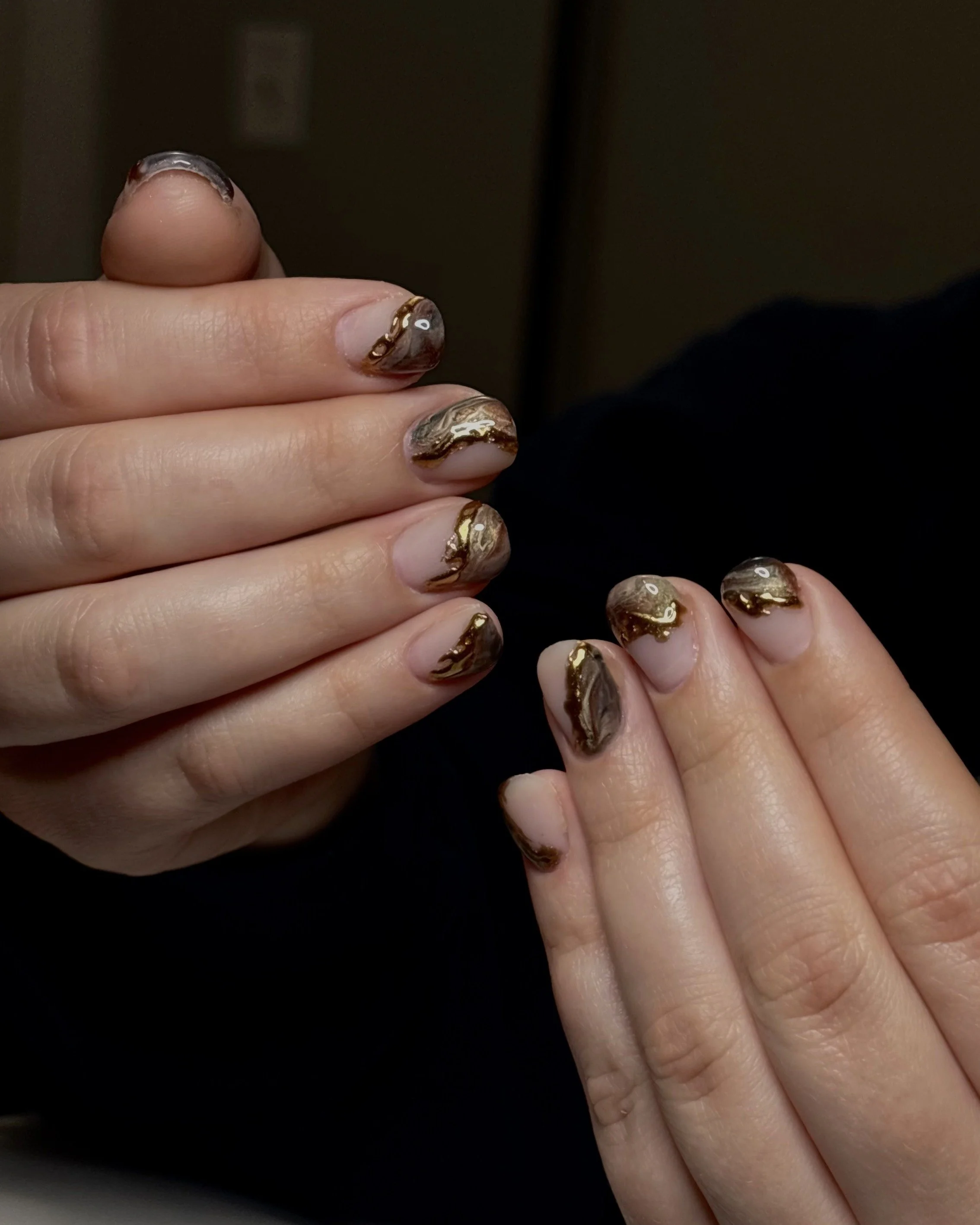 Close-up of a hand with gold and black marbled nail art on fingernails.