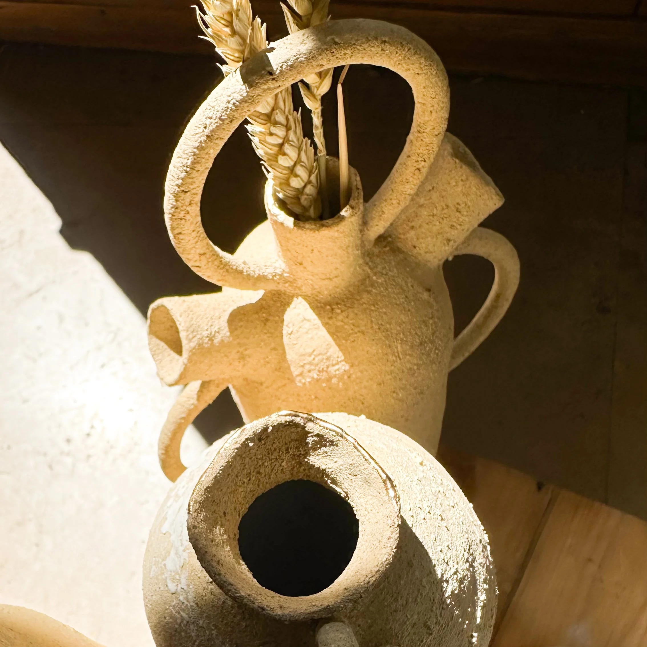 Vase en céramique avec une décoration en forme de cercle, contenant des feuilles ou fleurs séchées, placé sur une surface en bois, avec un éclairage chaud.