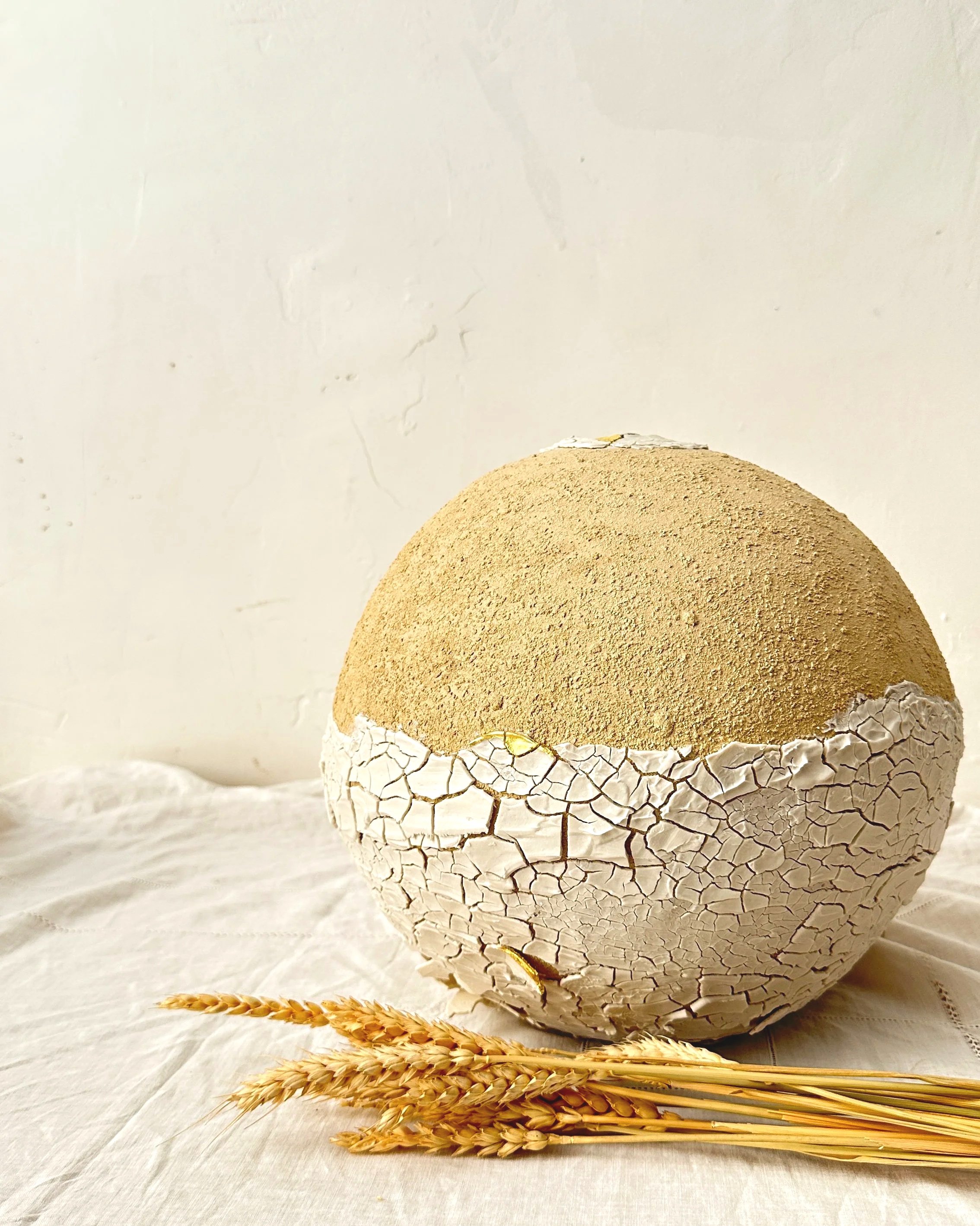 Vase boule Moon jar avec une surface craquelée, semblable à une œuf ou un décor artisanal, placé sur une toile de fond claire avec des épis de blé en avant-plan.