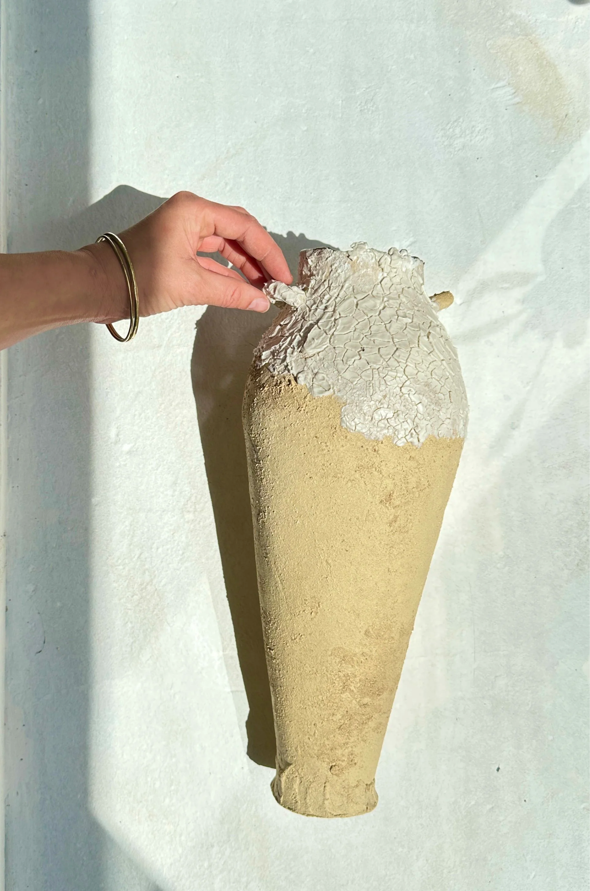 Vase en céramique beige avec texture craquelée blanche en haut, posé sur un fond blanc, éclairé par la lumière naturelle.