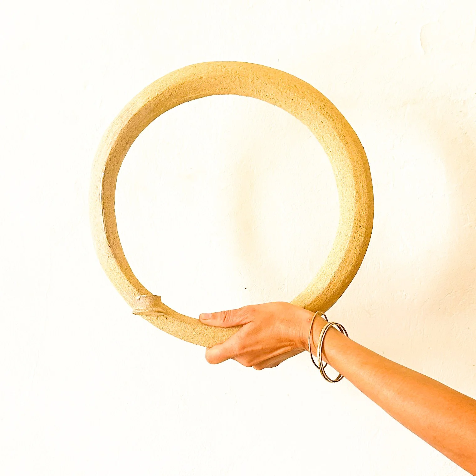 Une main tient un cadre circulaire beige devant un mur blanc.