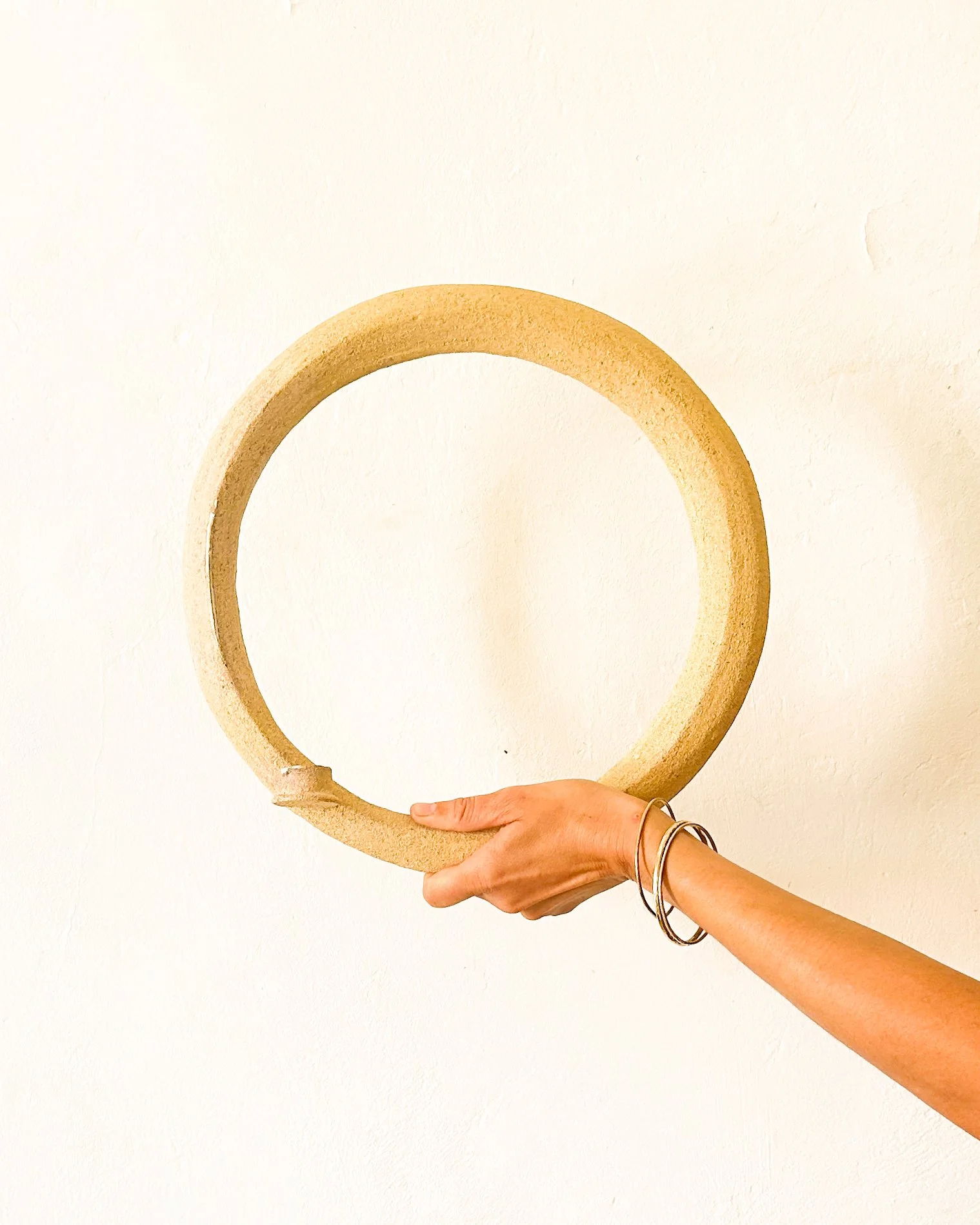 Une main tenant un cercle en bois contre un mur blanc.