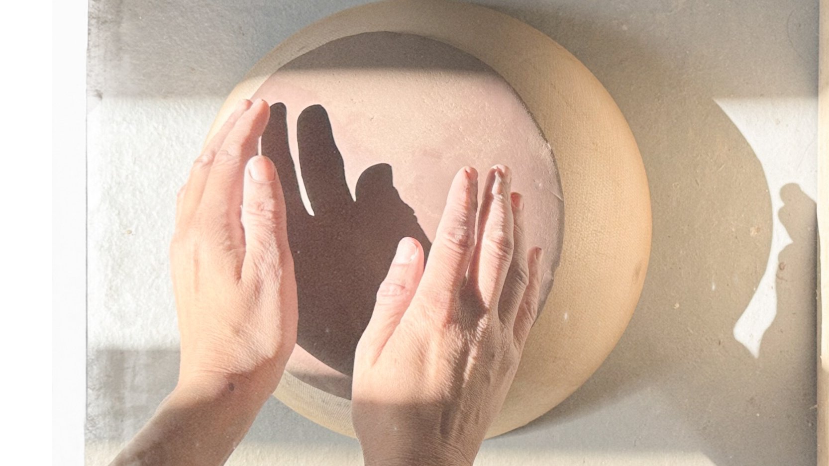 Deux mains posées sur une surface de tissu, créant une ombre en forme de main projetée sur un cercle découpé dans une feuille de papier