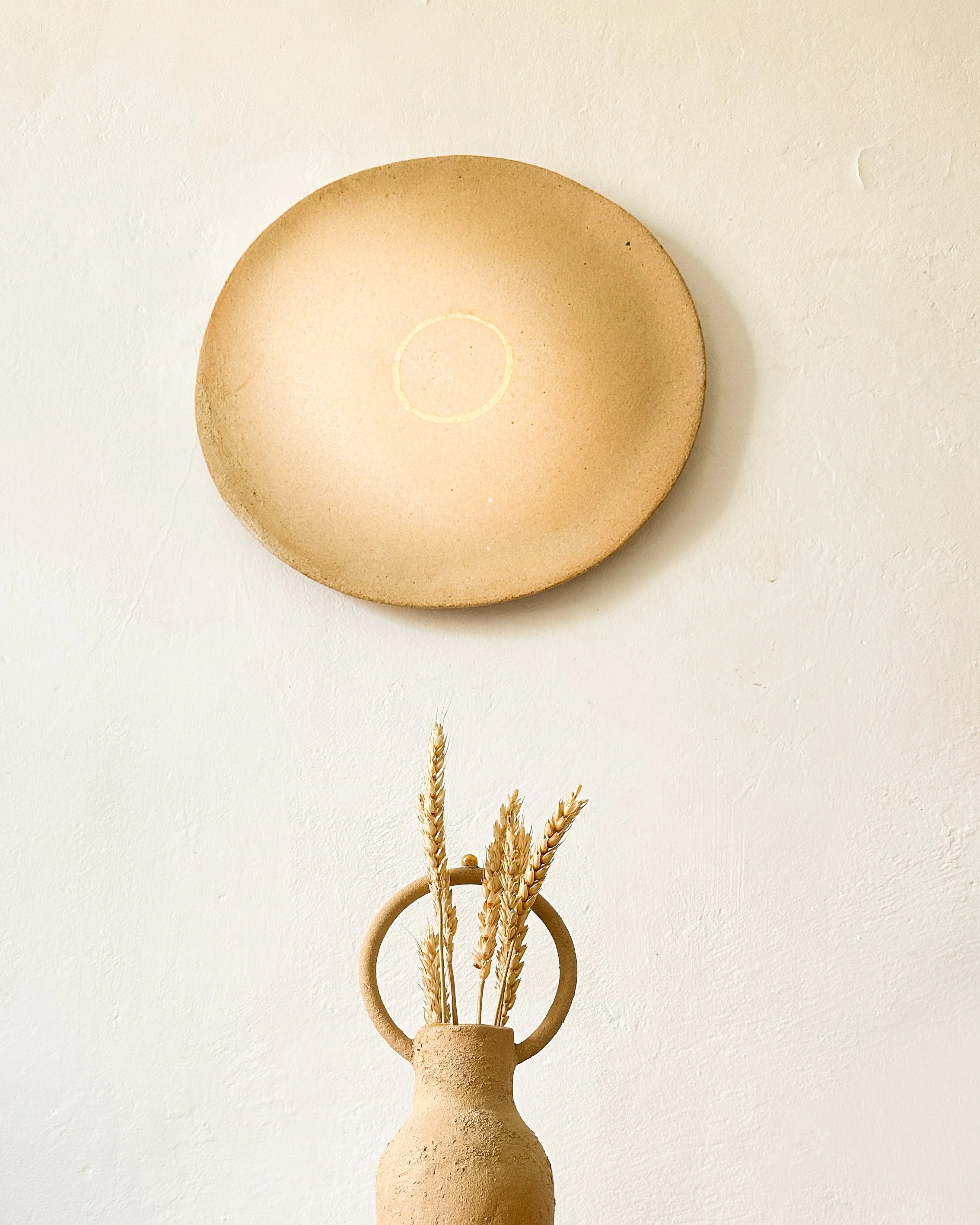 Vase en terre cuite beige avec des tiges de blé sec, décoration minimaliste sur fond blanc.
